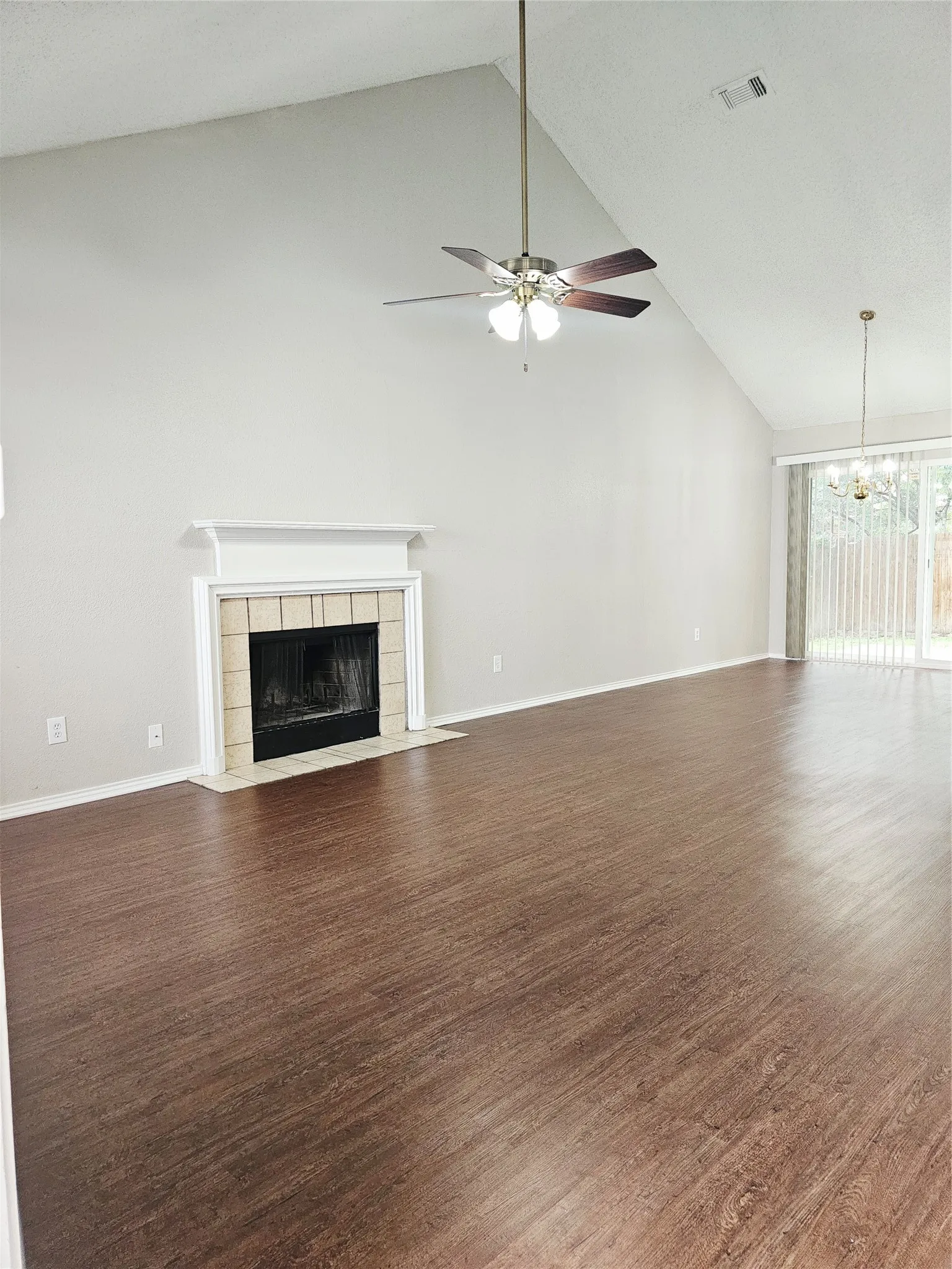 Spacious living area featuring high vaulted ceilings, wood-finish flooring, a central fireplace with mantle, and an overhead ceiling fan