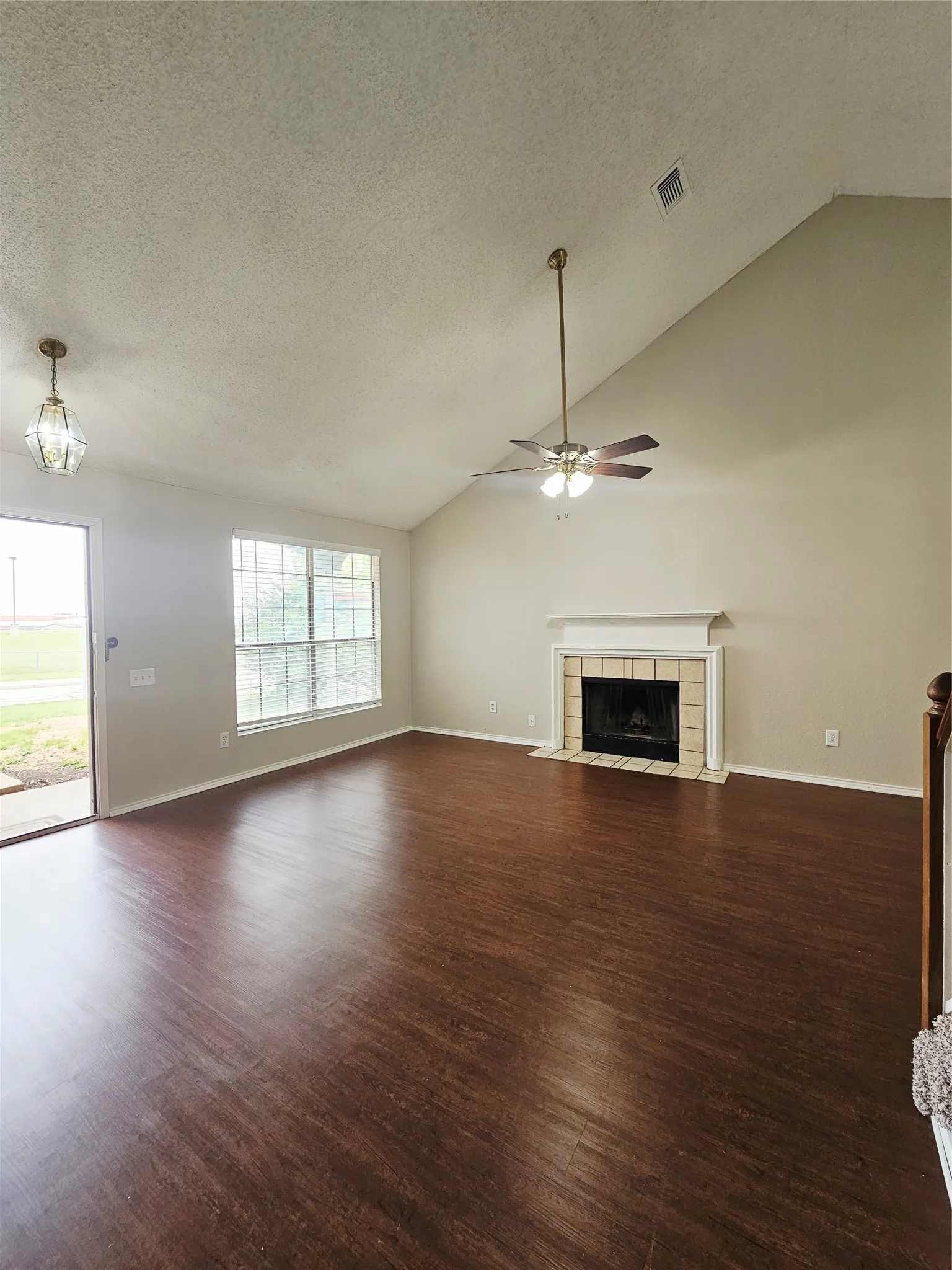Spacious living area featuring vaulted ceilings, wood-finish flooring, a fireplace with a tiled surround, a large window, and a glass-paneled door