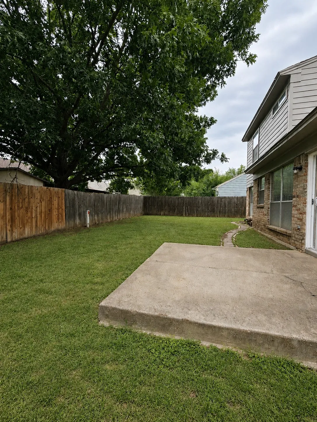 Private backyard with a mature tree, wood privacy fence, and a concrete patio