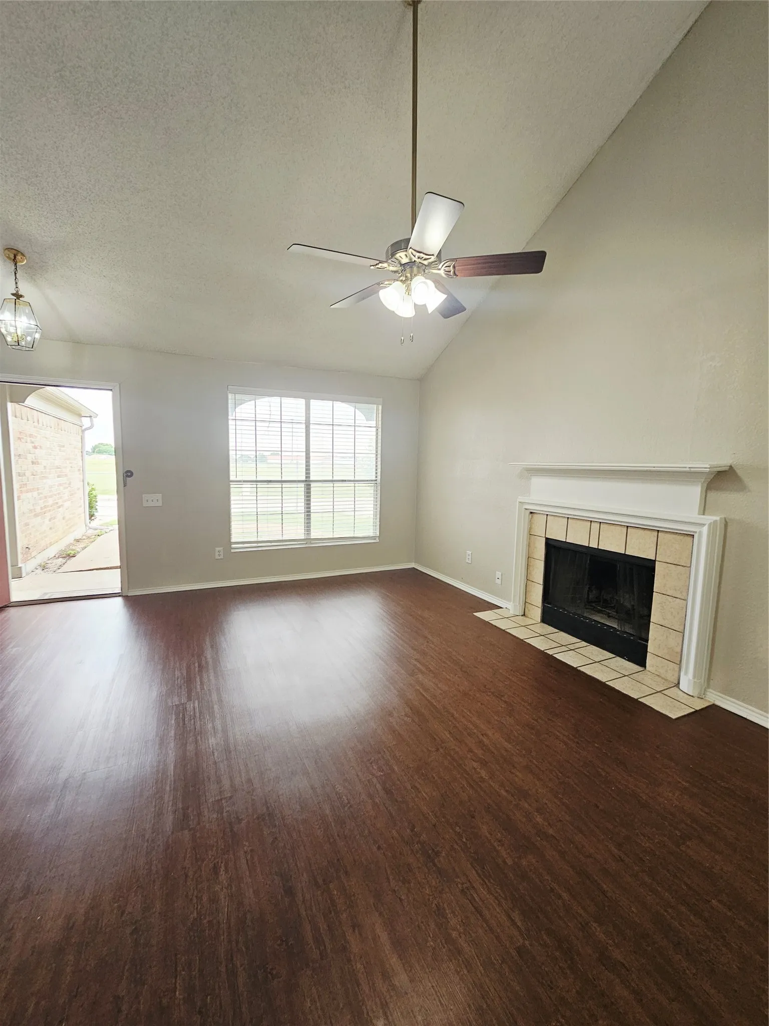 Spacious living area featuring wood-finish flooring, a vaulted ceiling, and a ceiling fan