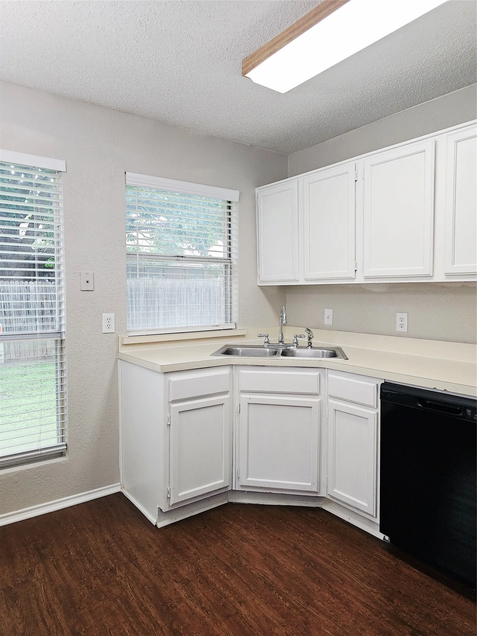 Kitchen featuring white cabinetry, light-toned countertops, a stainless steel double sink, and wood-finish flooring