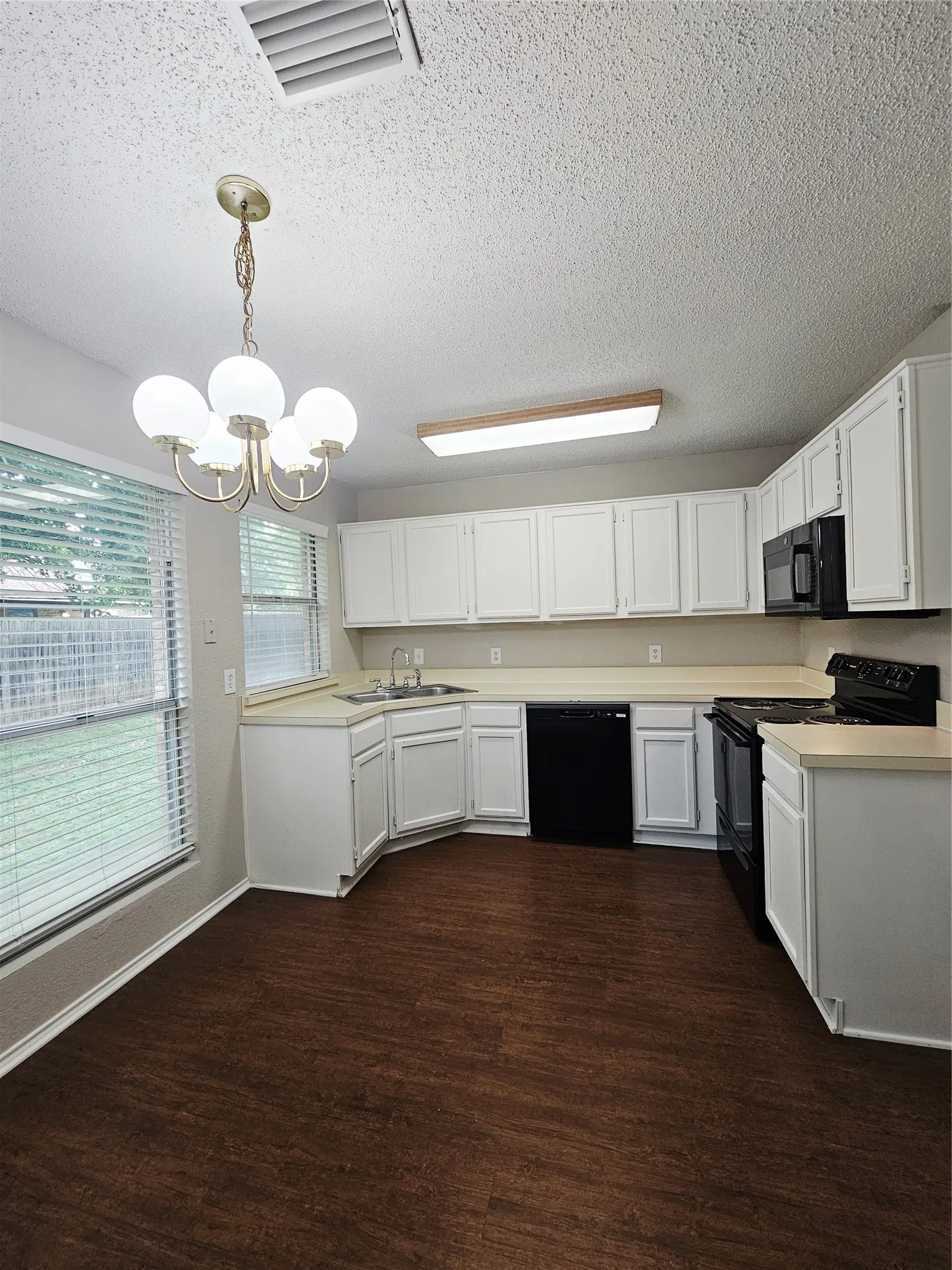 Kitchen featuring wood-finish flooring, white cabinetry, light-toned countertops, and black appliances