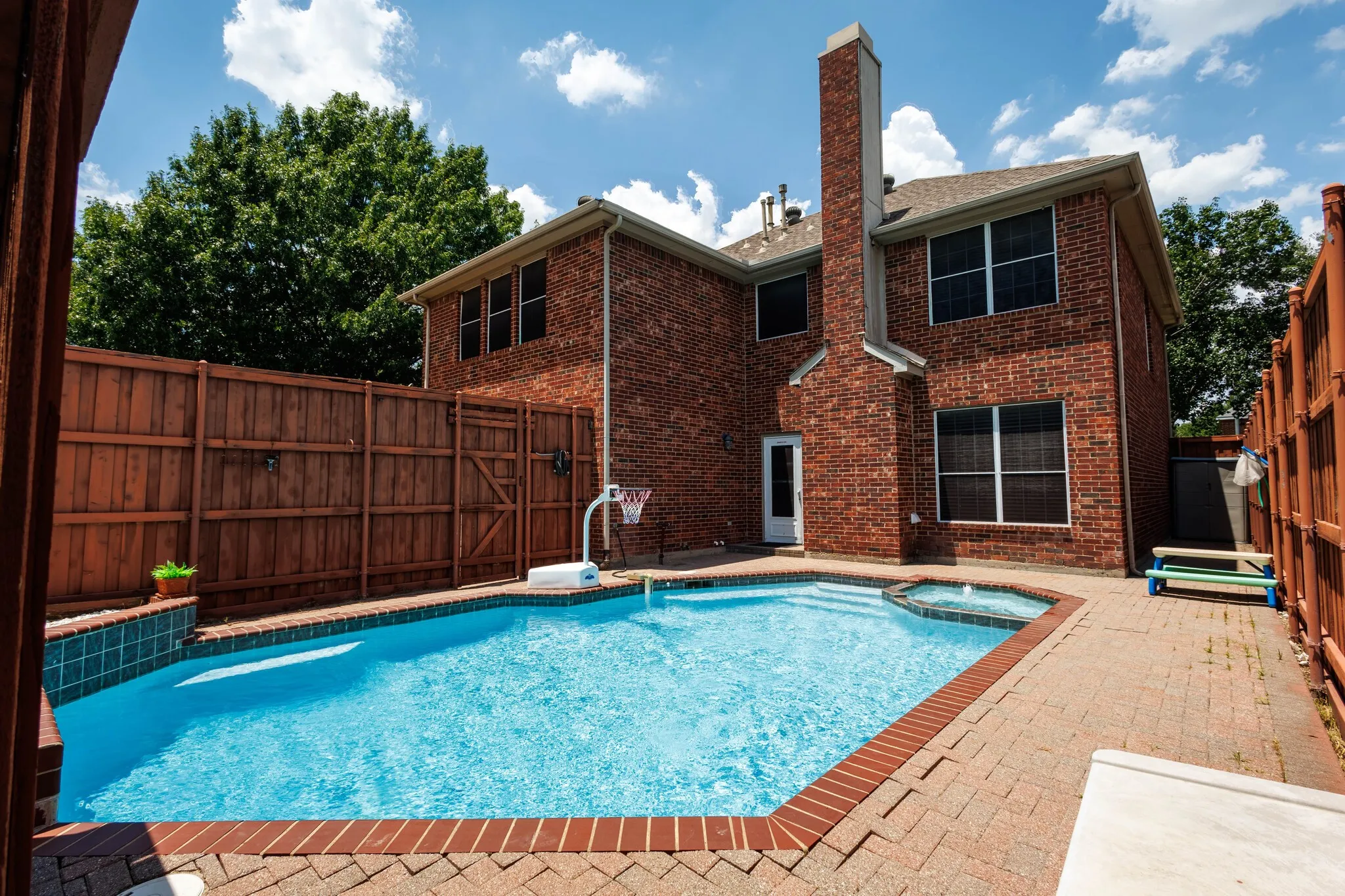 Private backyard featuring a swimming pool with integrated spa, brick paver patio, and full privacy fencing