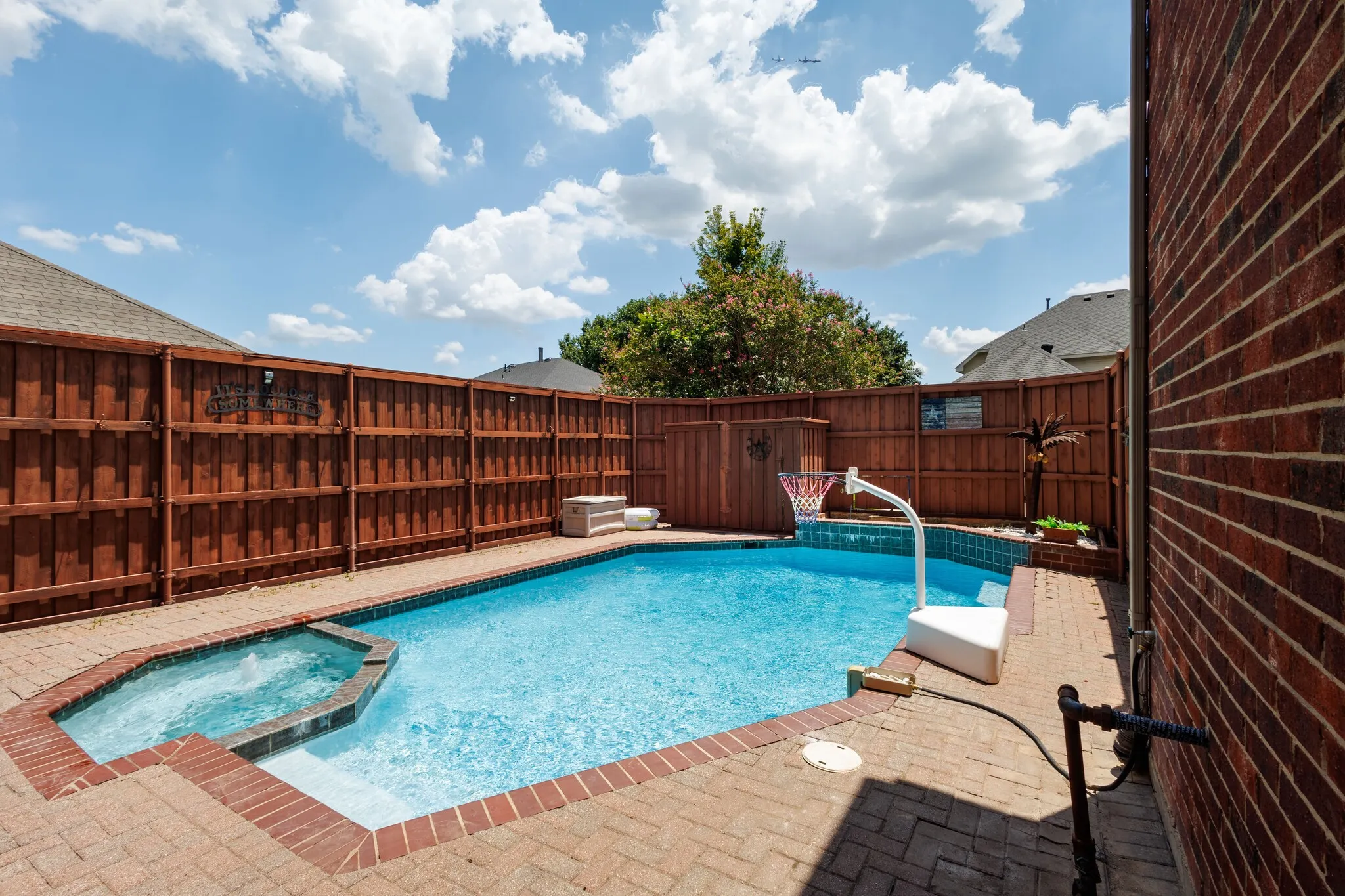 Private backyard featuring a swimming pool, integrated spa, and brick paver surround
