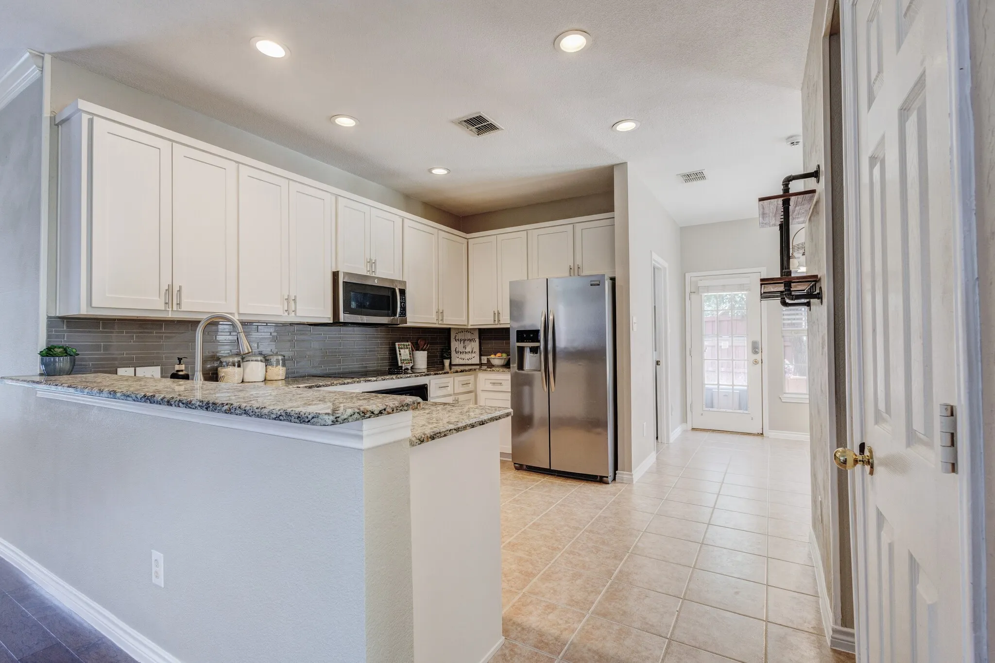 Kitchen featuring white cabinetry, granite countertops, a stainless steel refrigerator, and a tile backsplash