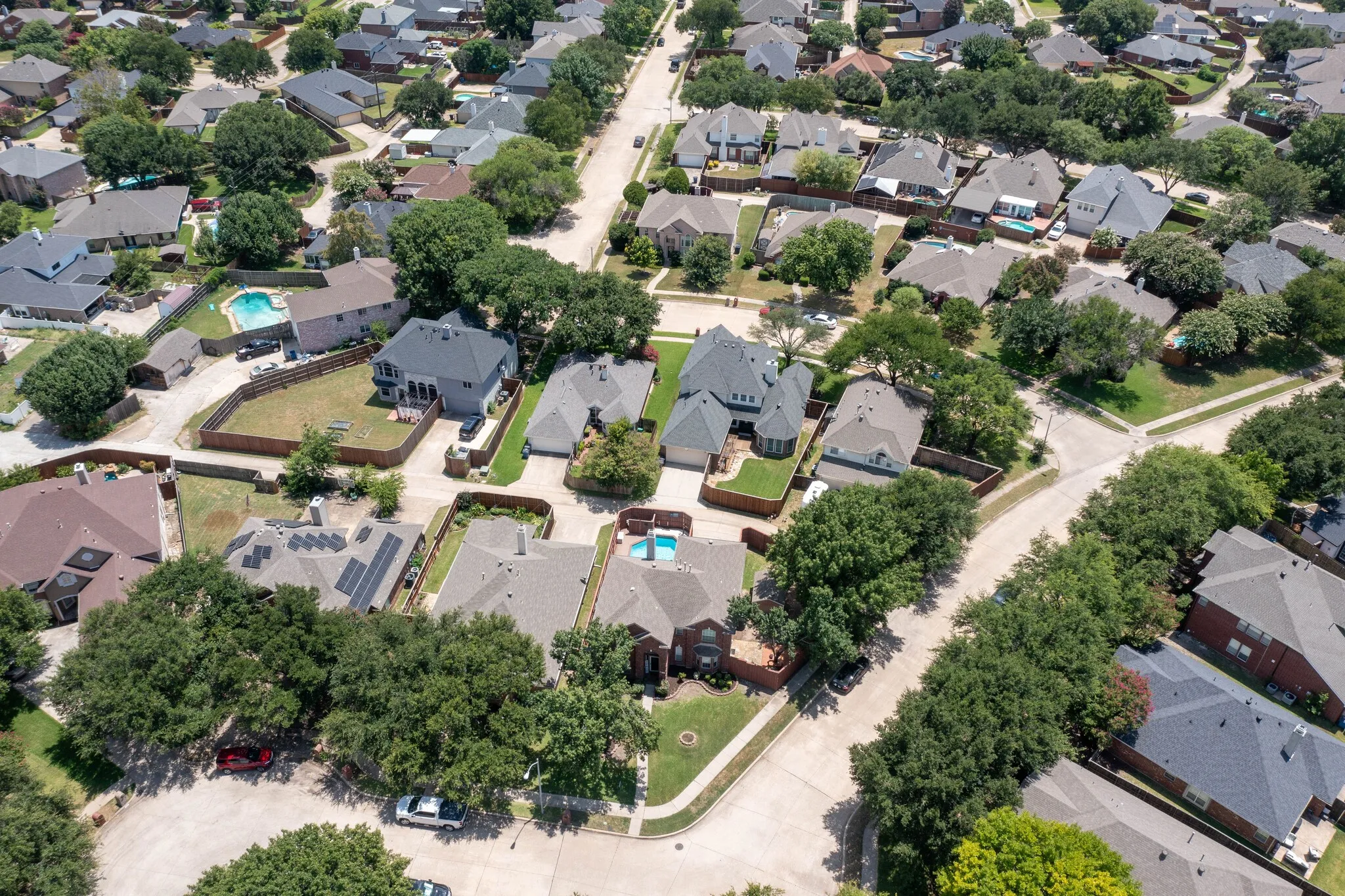 Residential neighborhood with mature trees, visible pools, and a mix of roof styles including some with solar panels