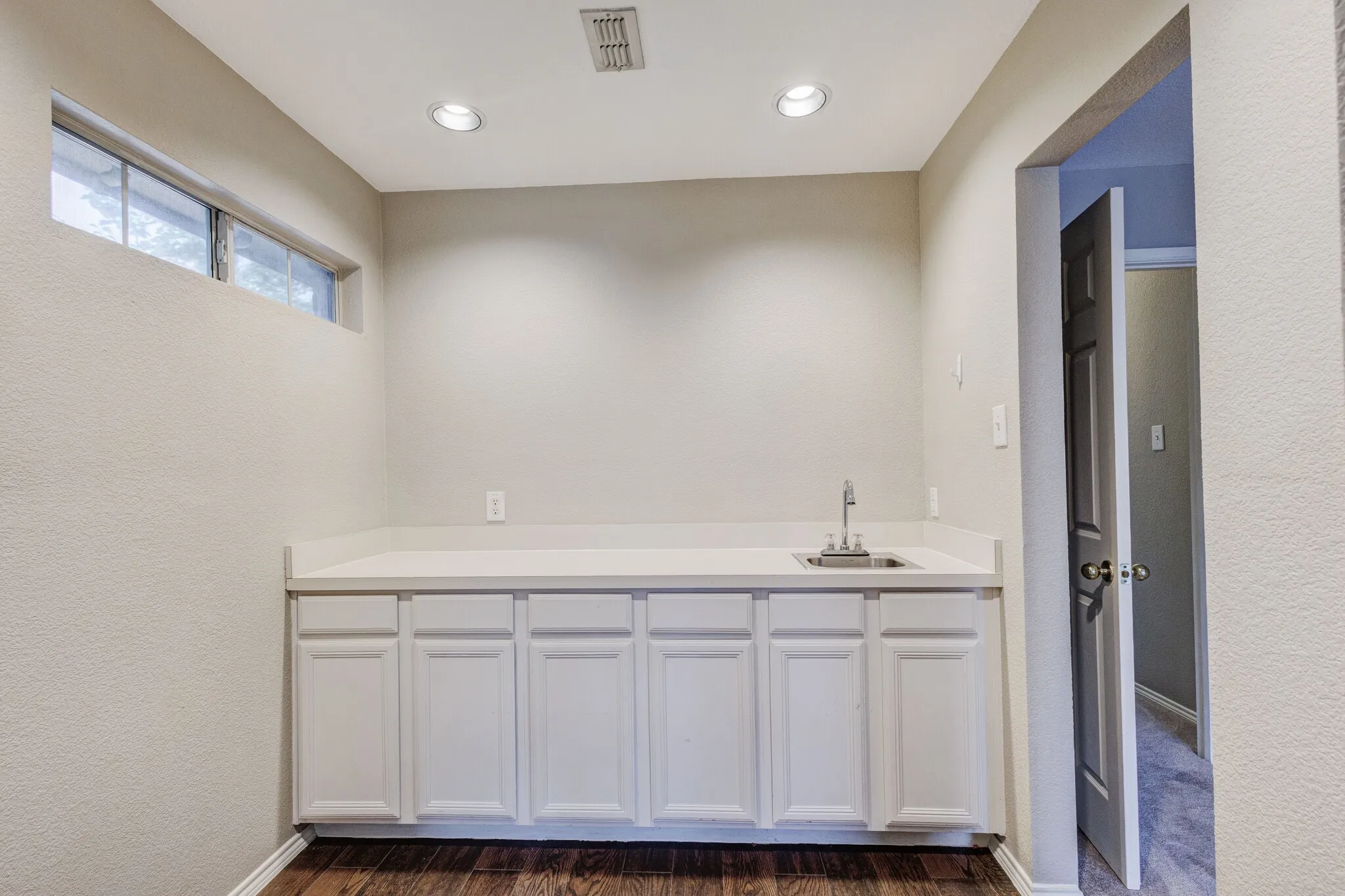 Wet bar featuring white cabinetry, a solid surface countertop, stainless steel sink, and chrome faucet