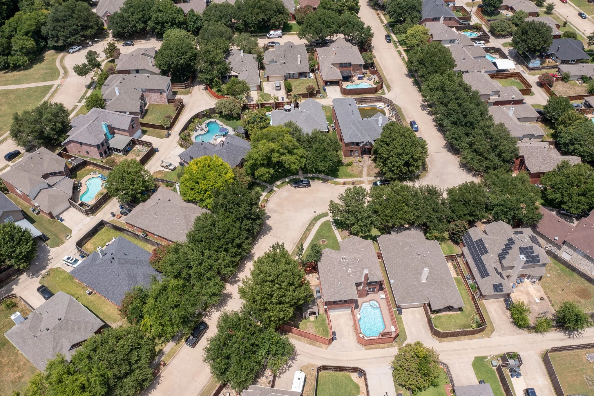 Aerial view highlighting a residential neighborhood with mature trees and multiple properties featuring private swimming pools