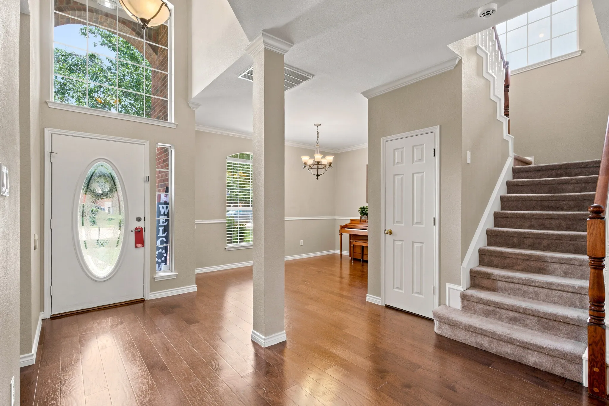 Two-story foyer with wood-finish flooring, a white front door featuring an oval glass insert, and a transom window