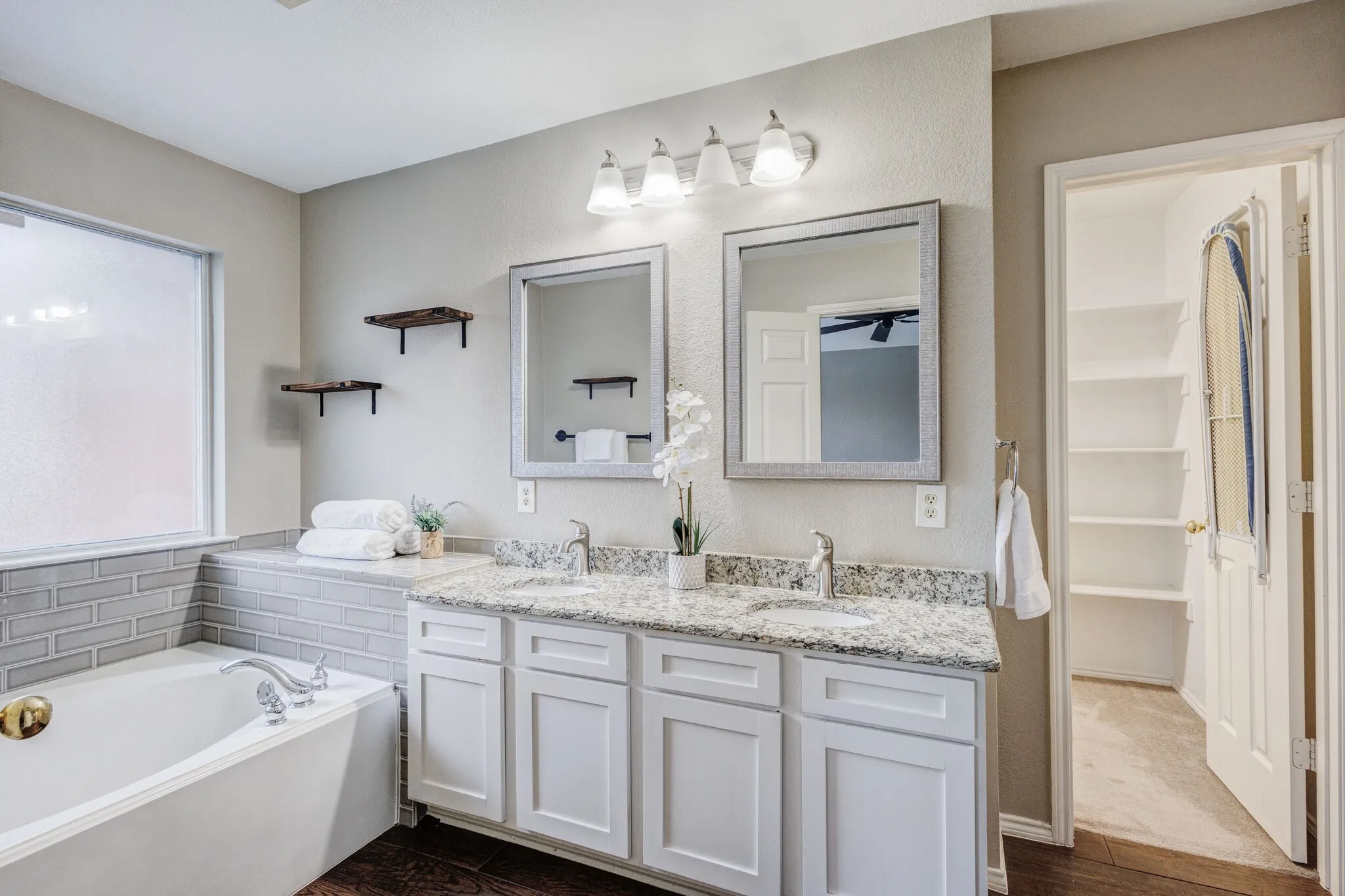 Bathroom featuring a built-in soaking tub with subway tile surround, a dual vanity with white cabinetry and stone countertops, two framed mirrors, and overhead vanity lighting