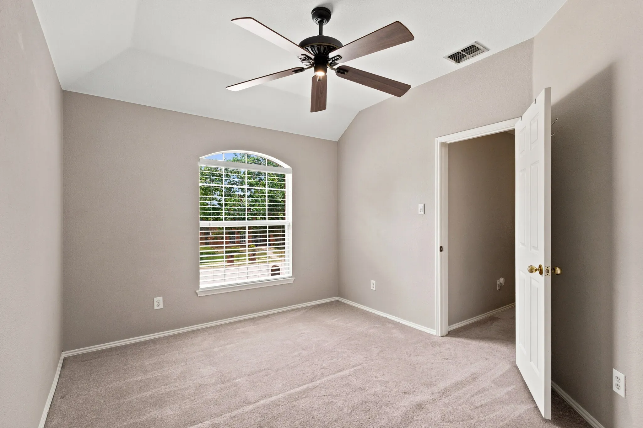 Room featuring a vaulted ceiling, arched window with horizontal blinds, overhead ceiling fan with light fixture, neutral carpet flooring, and a six-panel interior door