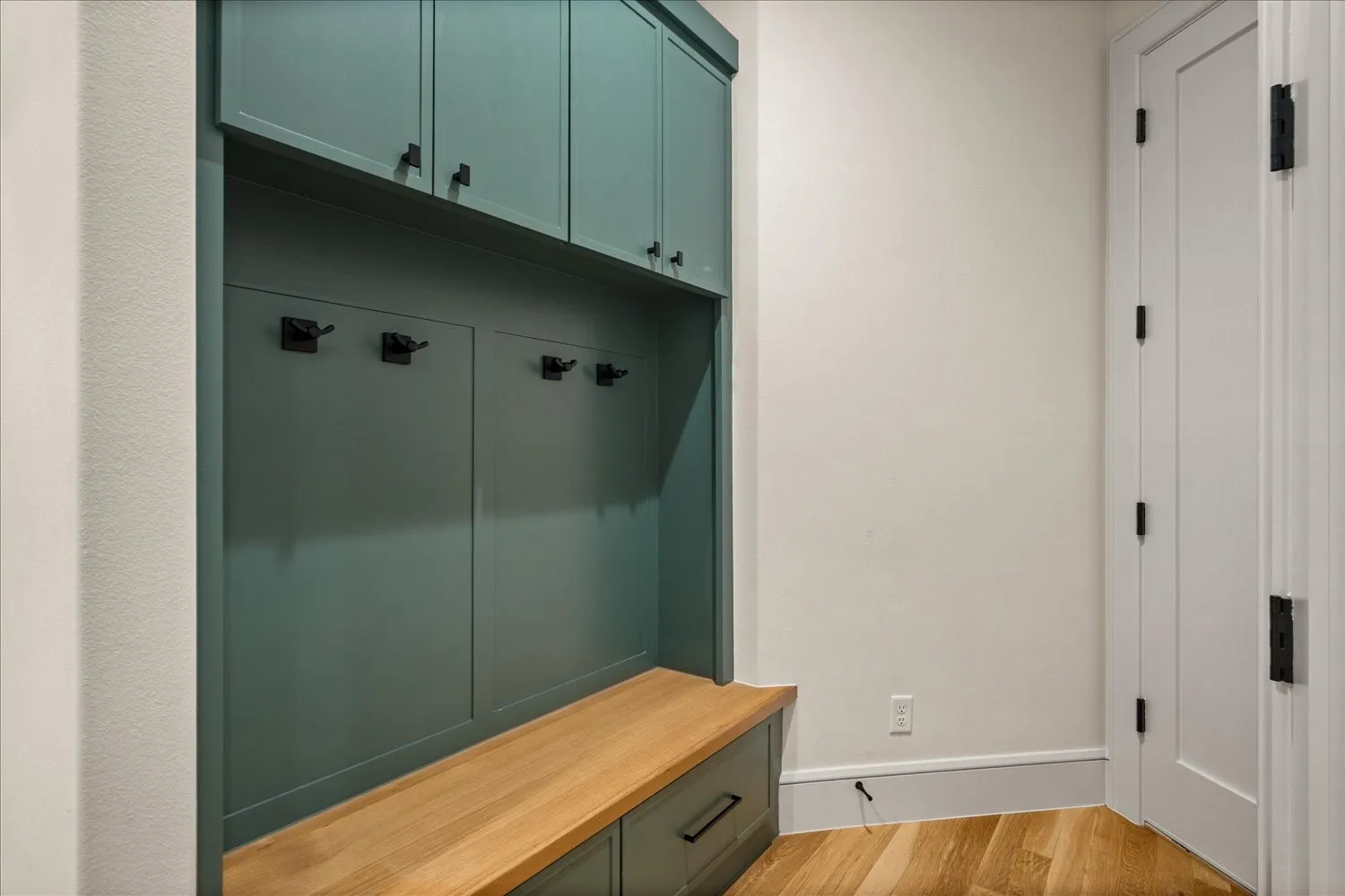 Built-in entryway storage featuring teal cabinetry, a wooden bench, and black hardware
