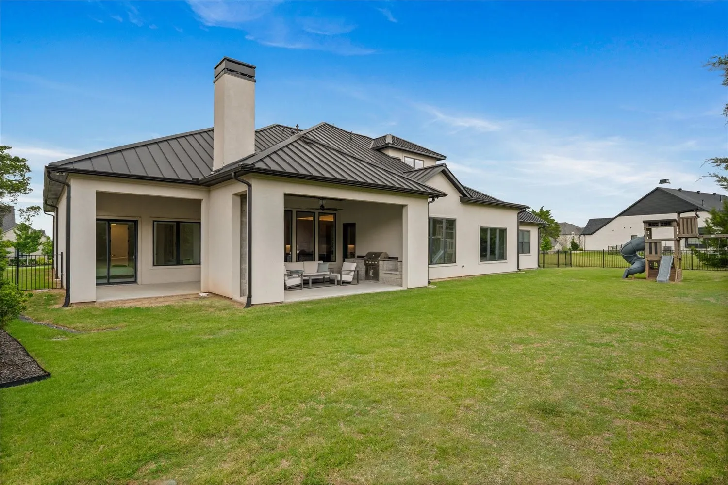 Expansive rear exterior featuring a covered patio, a charcoal metal roof, and a stucco finish
