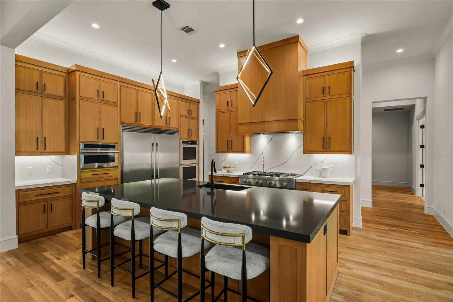 Gourmet kitchen featuring custom wood cabinetry, stainless steel appliances, a center island with a dark countertop, elegant pendant lighting, and light wood flooring