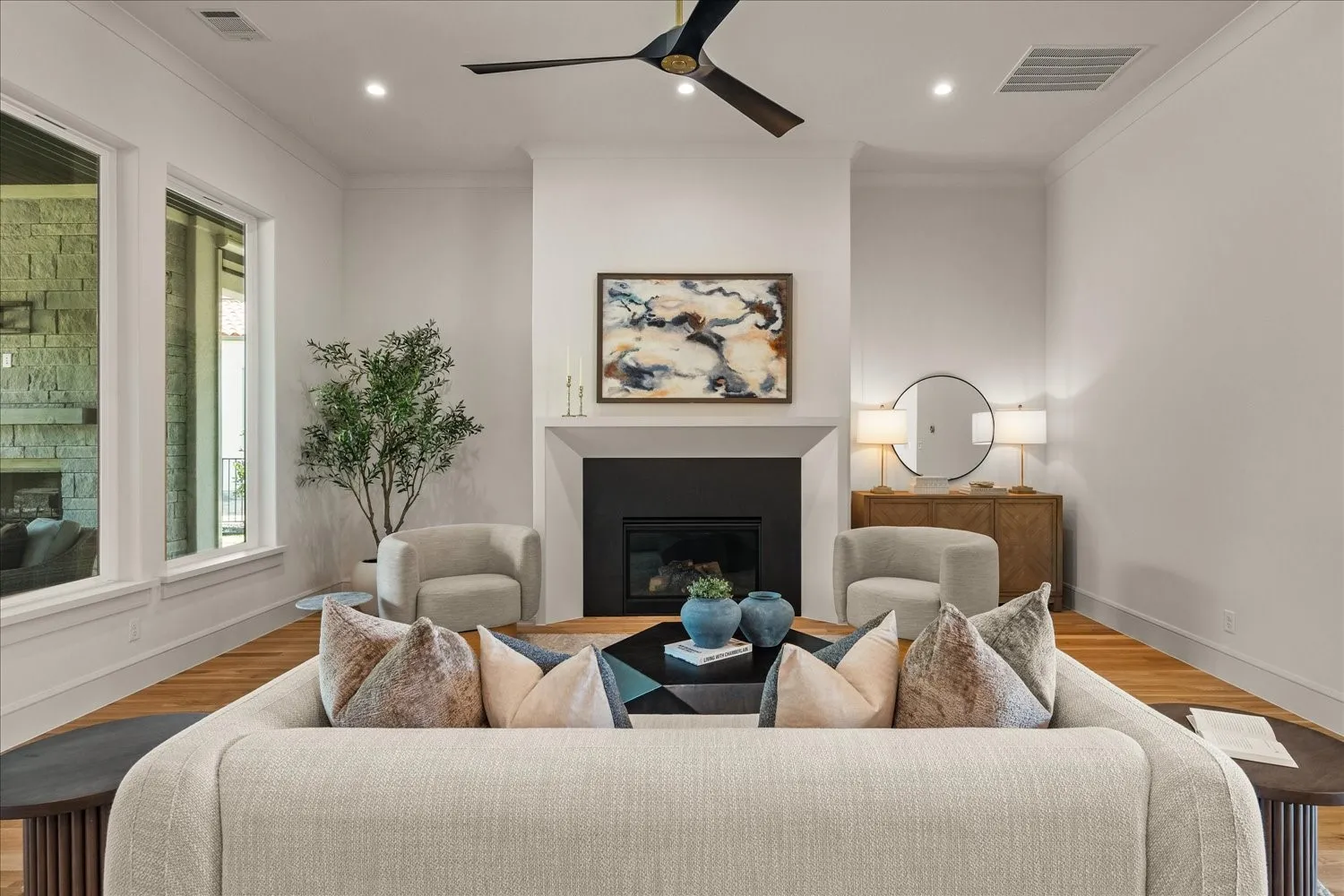 Spacious living area featuring a fireplace with a dark surround, wood-finish flooring, recessed lighting, a ceiling fan, and large windows