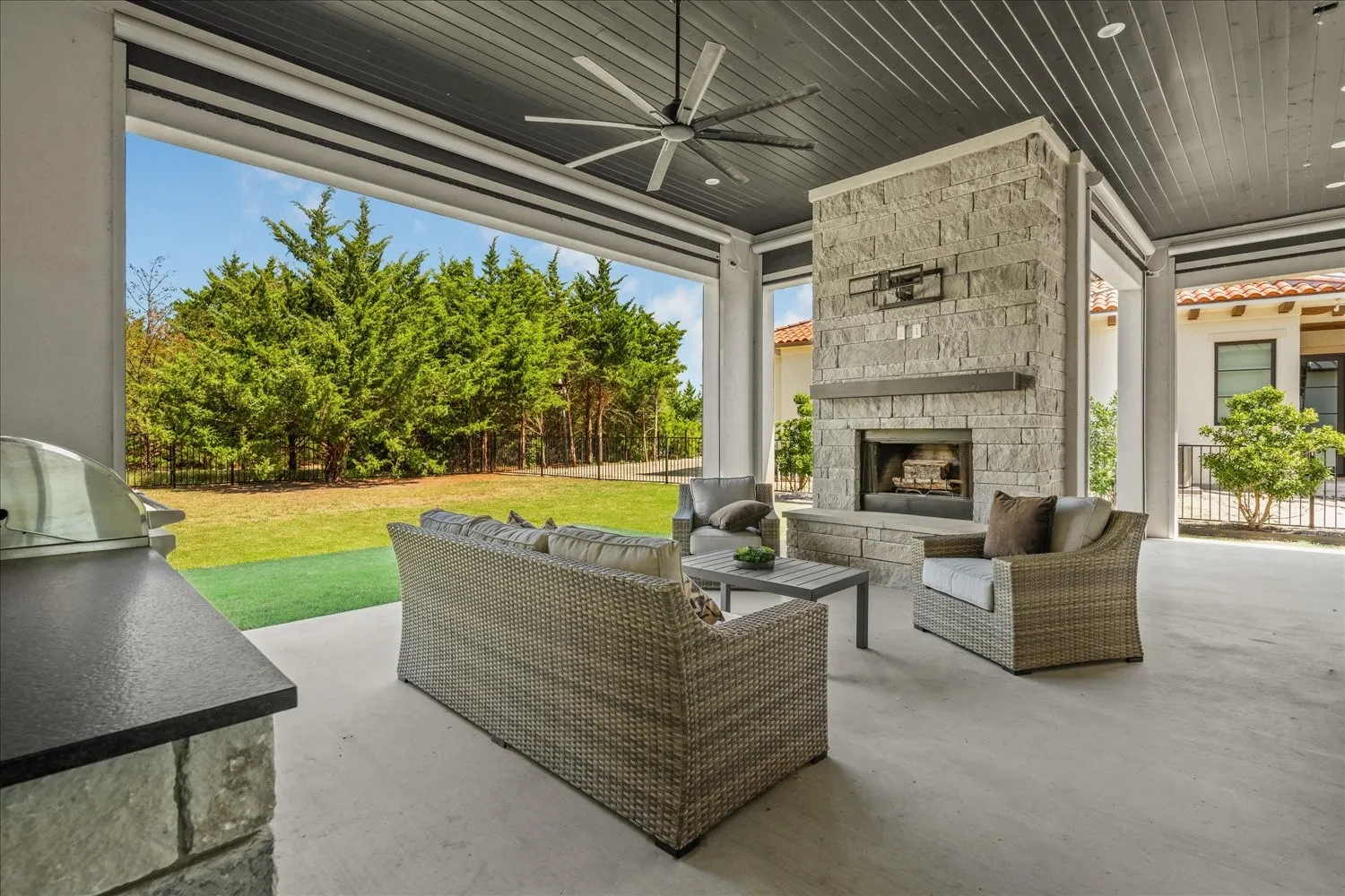Expansive covered patio featuring a stone fireplace, built-in outdoor grill, dark wood-finish ceiling, and a large ceiling fan