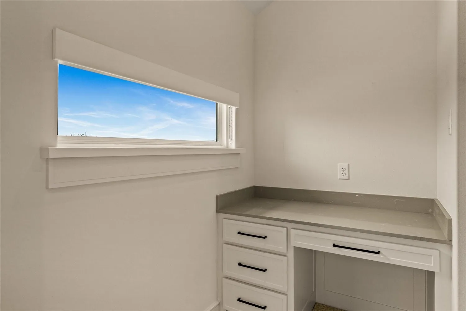 Built-in desk area featuring light cabinetry, dark hardware, and a solid surface countertop