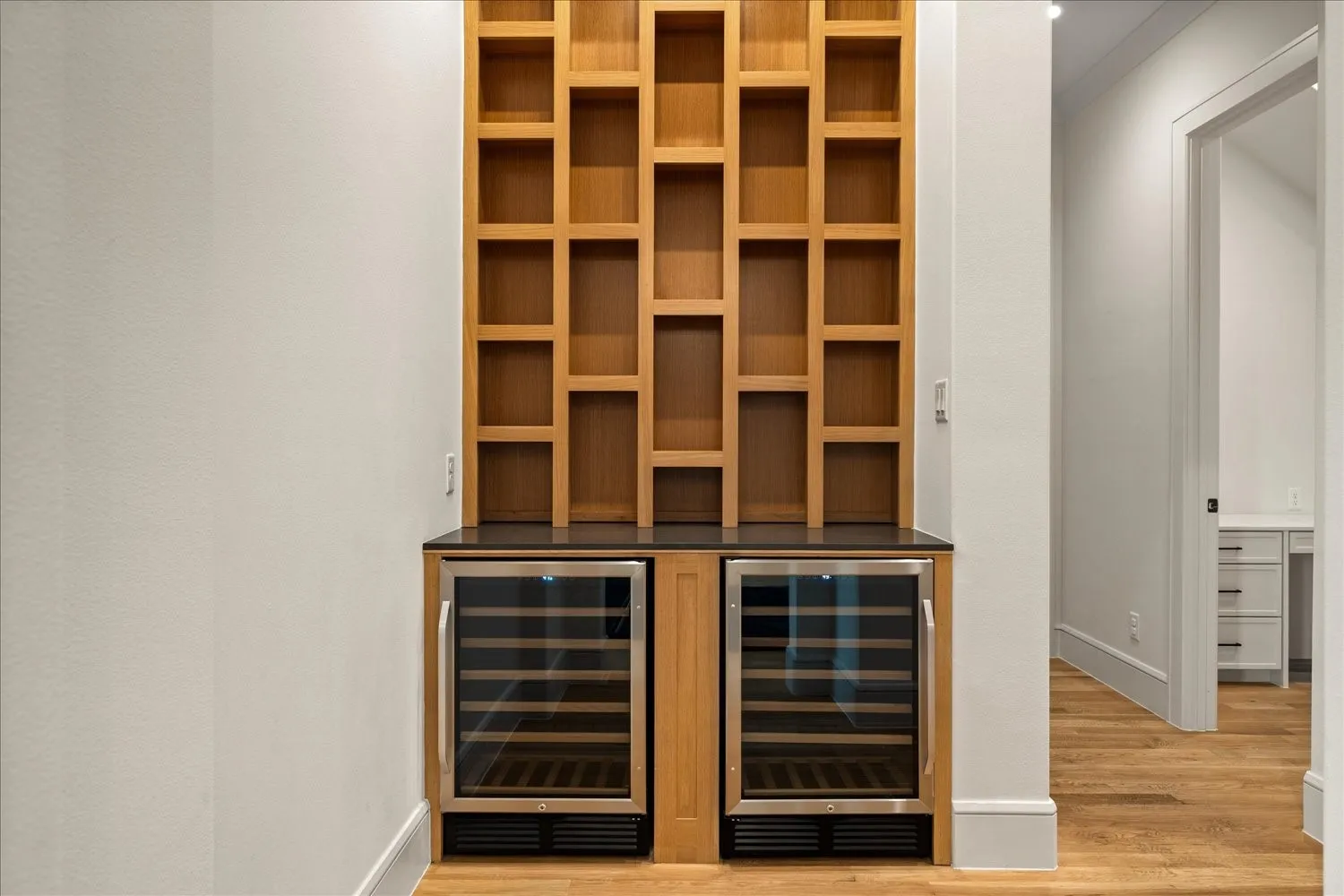 Built-in dry bar featuring two undercounter wine refrigerators, a dark countertop, and extensive wood shelving