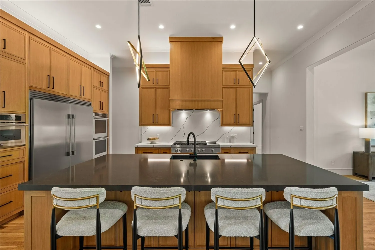 Expansive kitchen island with a dark countertop, wood-finish cabinetry, stainless steel appliances, and a tiled backsplash
