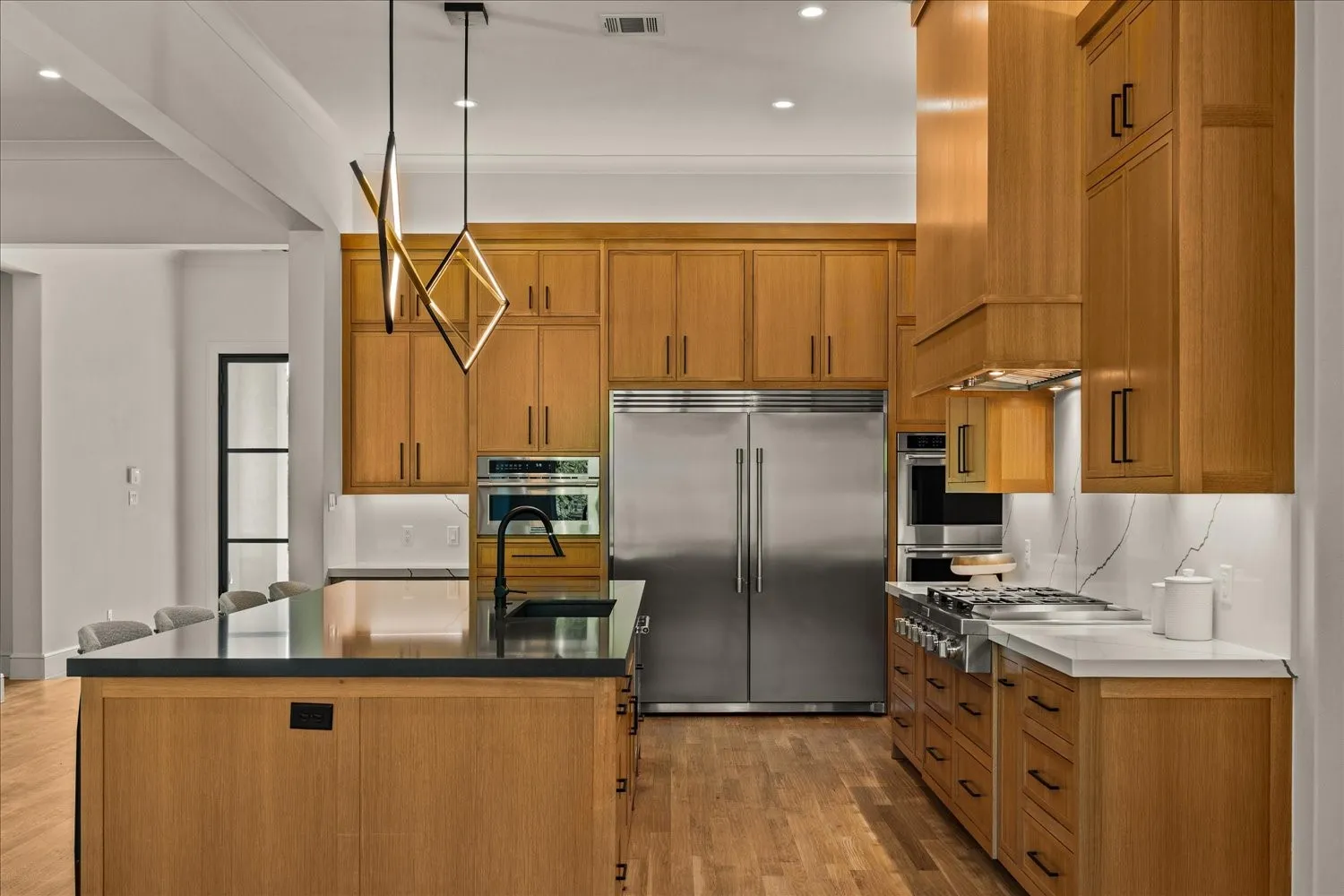 Kitchen featuring wood cabinetry, stainless steel appliances, a center island with a black countertop, and contemporary pendant lighting