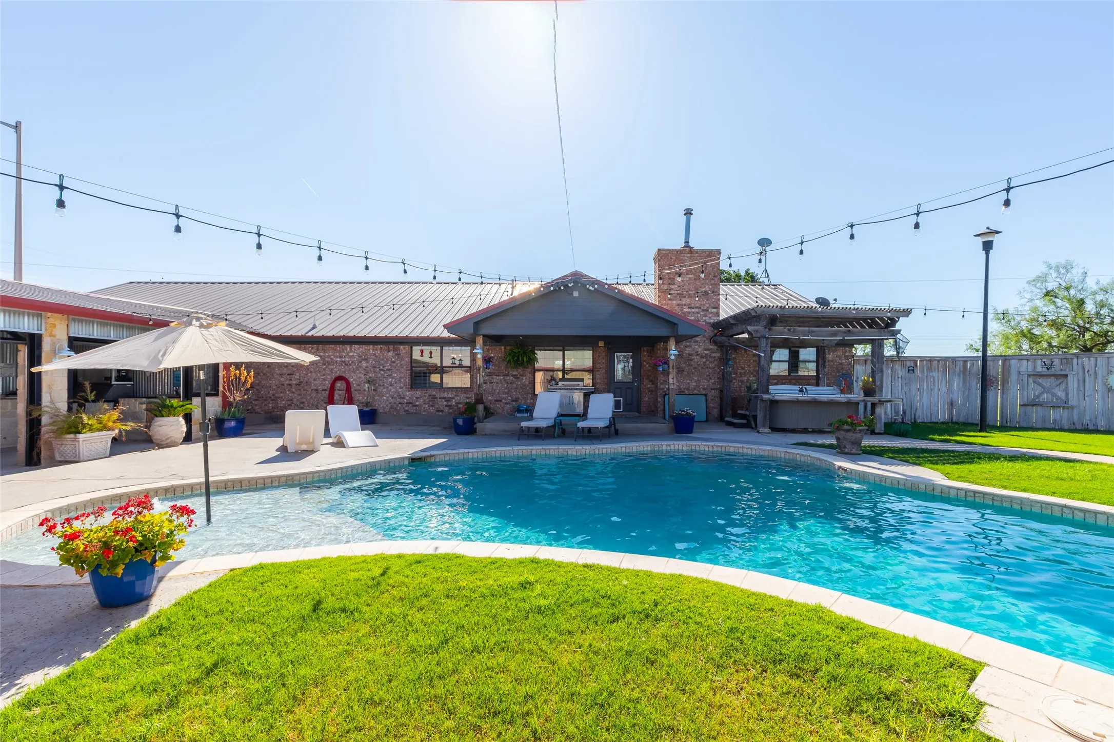 Backyard entertaining area featuring a curved swimming pool, extensive concrete patio, and lush green lawn
