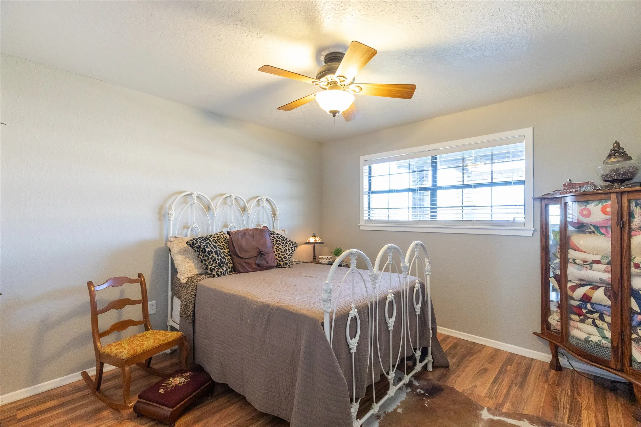 Room featuring wood-finish flooring, a ceiling fan with light fixture, and a window with blinds