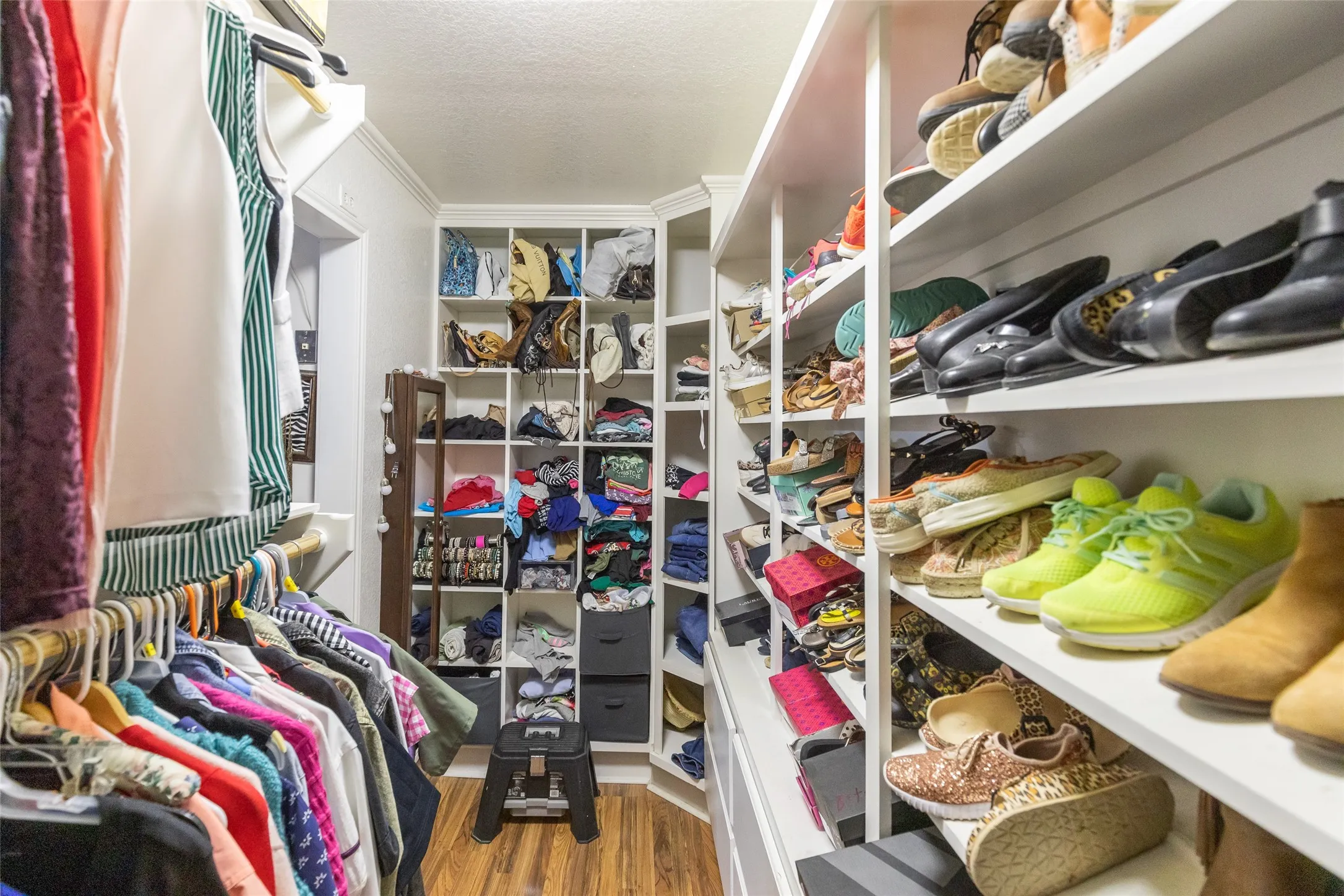 Custom closet featuring extensive built-in shelving, hanging rods, cubby storage, and wood-finish flooring