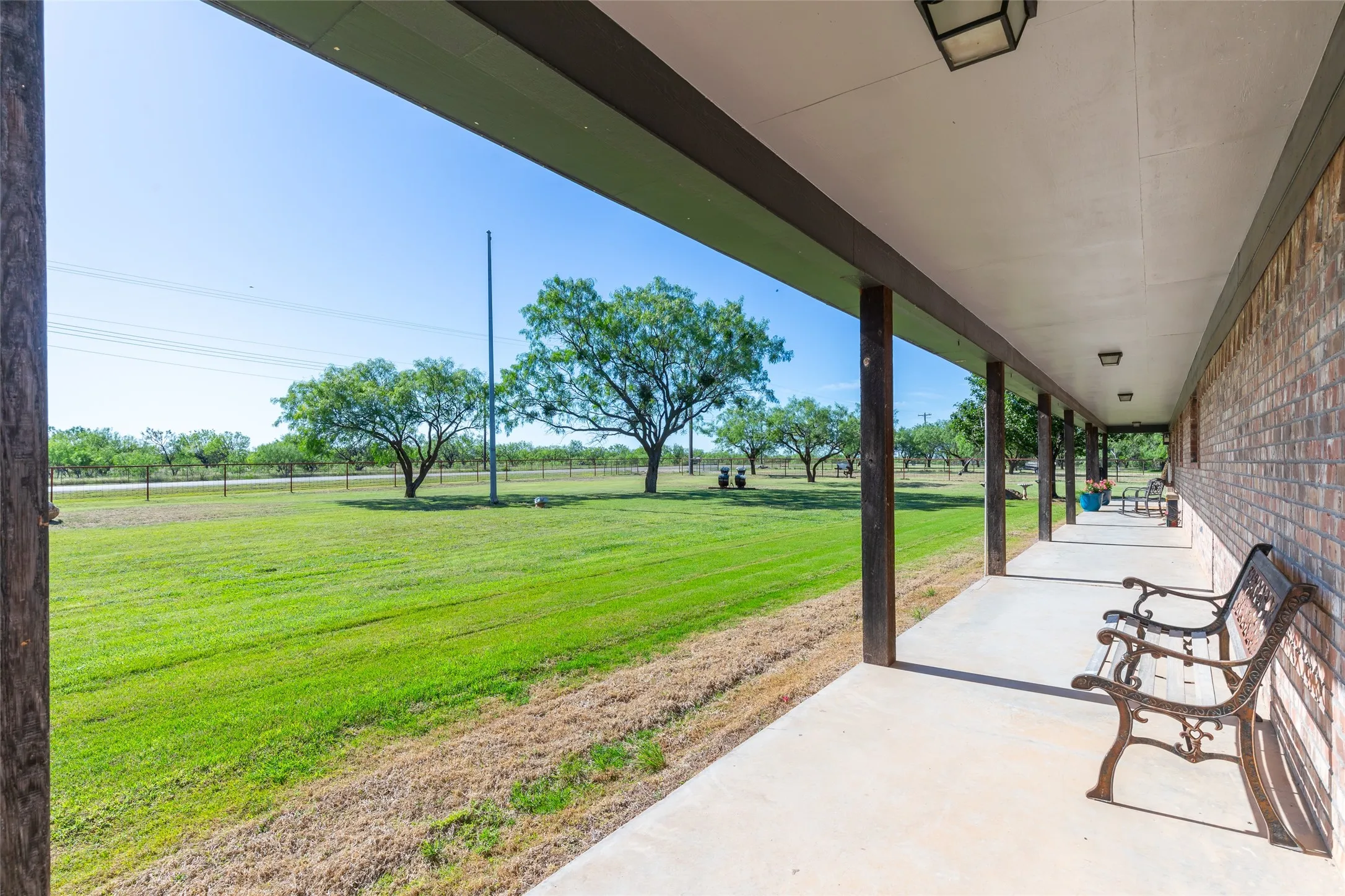 Expansive covered porch featuring a concrete surface, exposed support beams, and a brick exterior wall