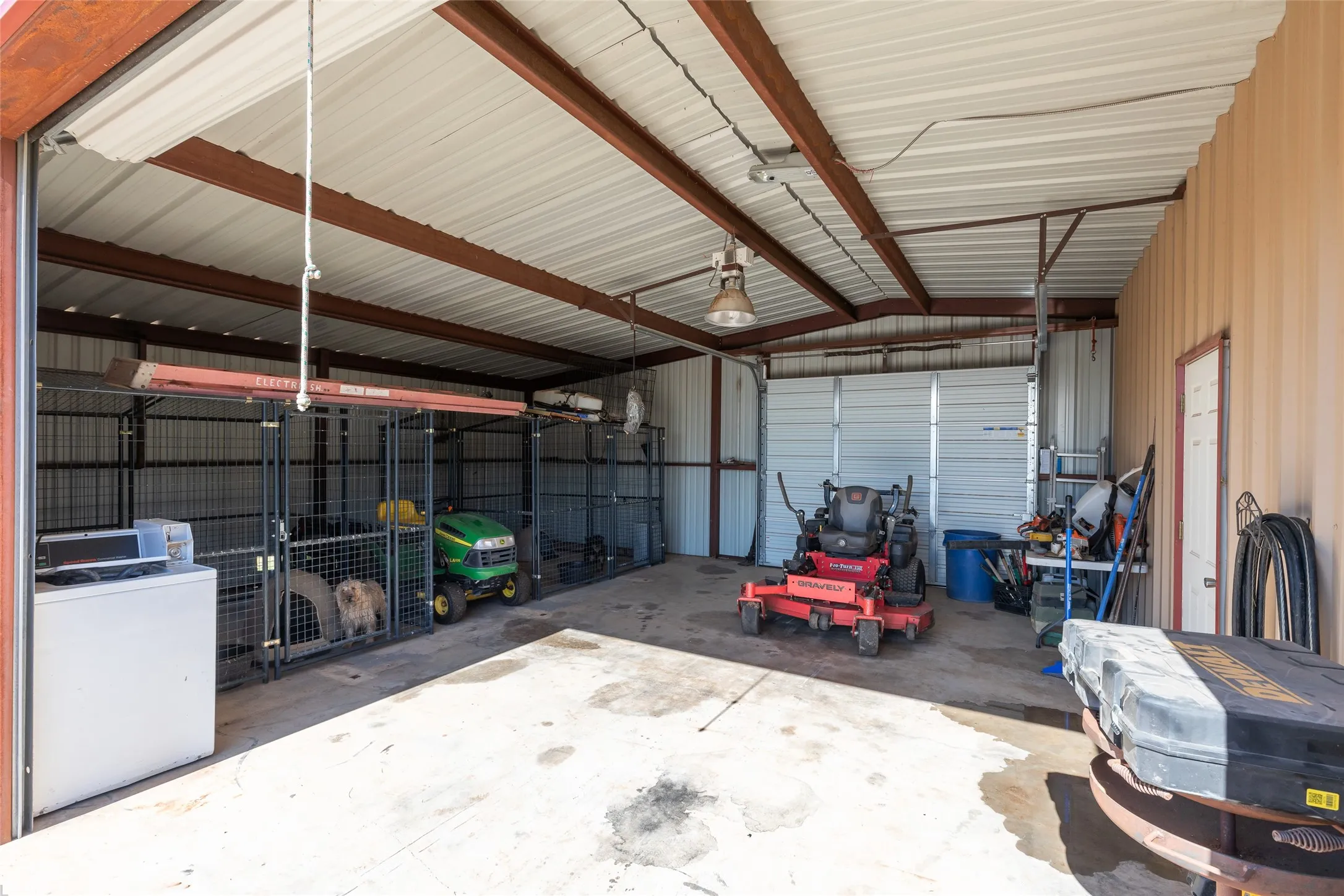 Expansive metal outbuilding featuring concrete flooring, exposed beam ceiling, corrugated metal siding, and a roll-up garage door