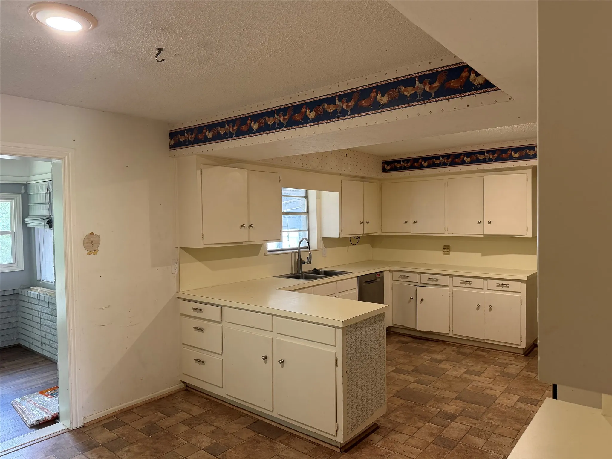 U-shaped kitchen featuring white cabinetry, light countertops, and a stainless steel dishwasher