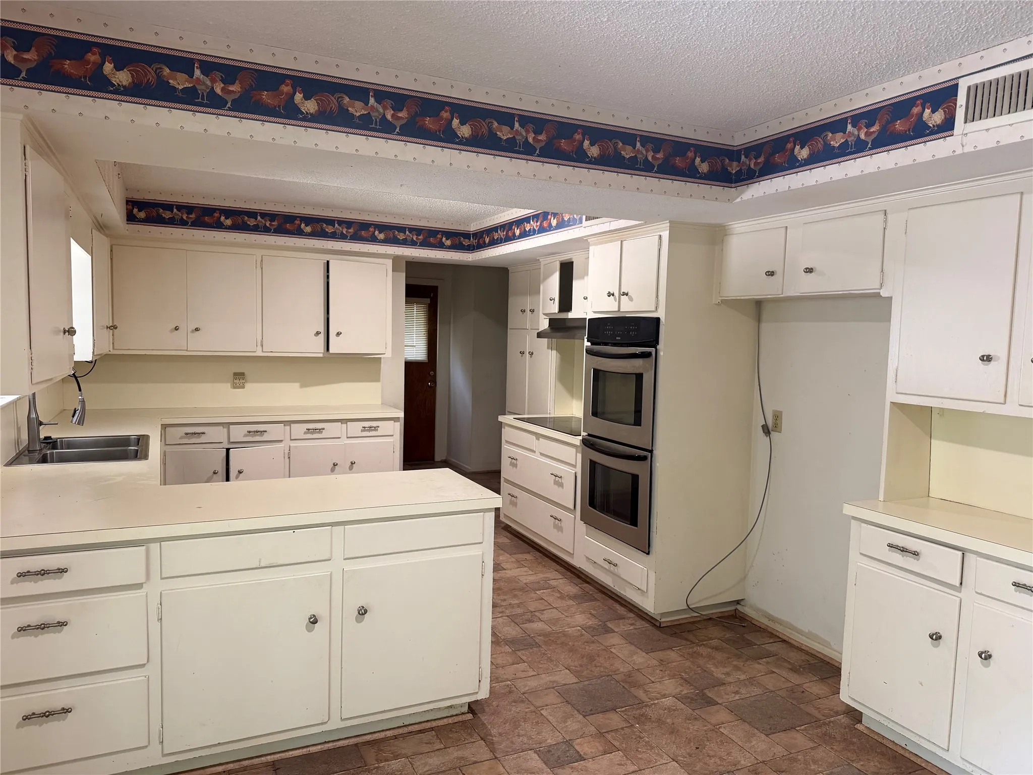 Spacious kitchen featuring white cabinetry, a kitchen island, double wall ovens, a built-in cooktop, and a stainless steel range hood