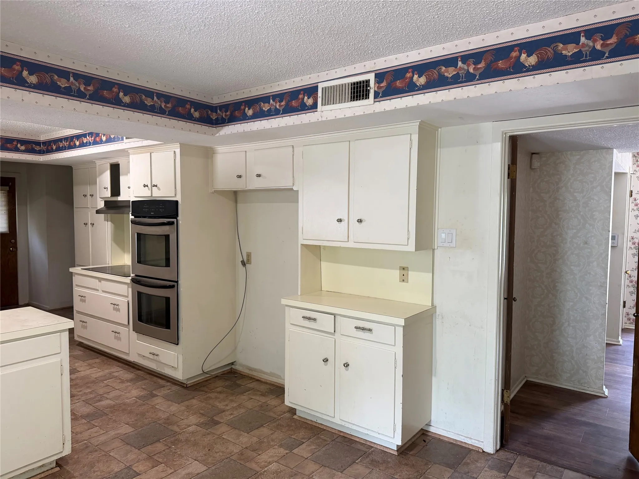 Kitchen featuring white cabinetry, integrated double ovens, and a built-in range hood