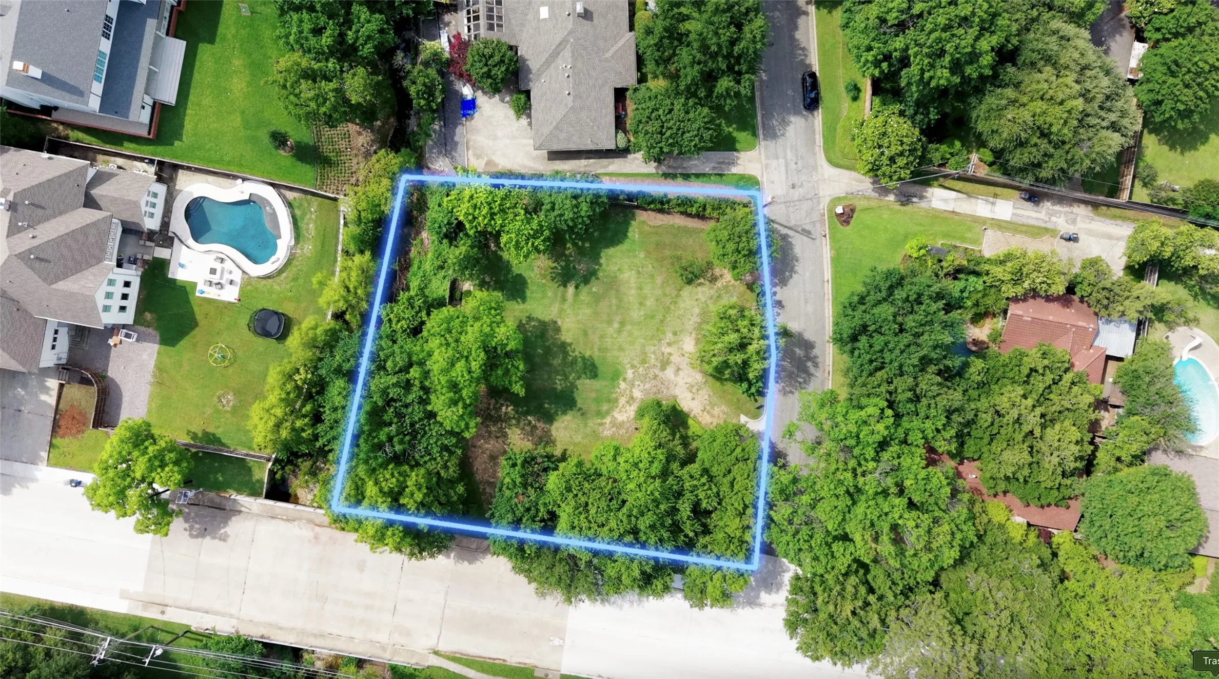 Vacant lot featuring established trees and a cleared central area, situated at a street intersection