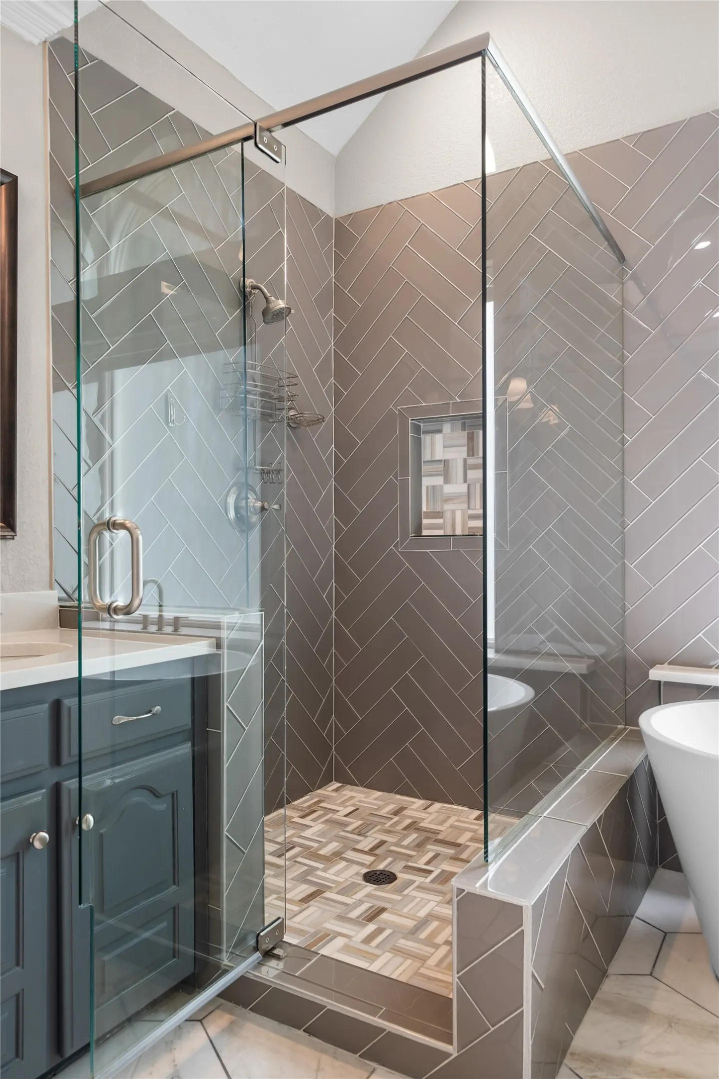 Glass-enclosed shower featuring herringbone-patterned wall tile and a mosaic tile floor