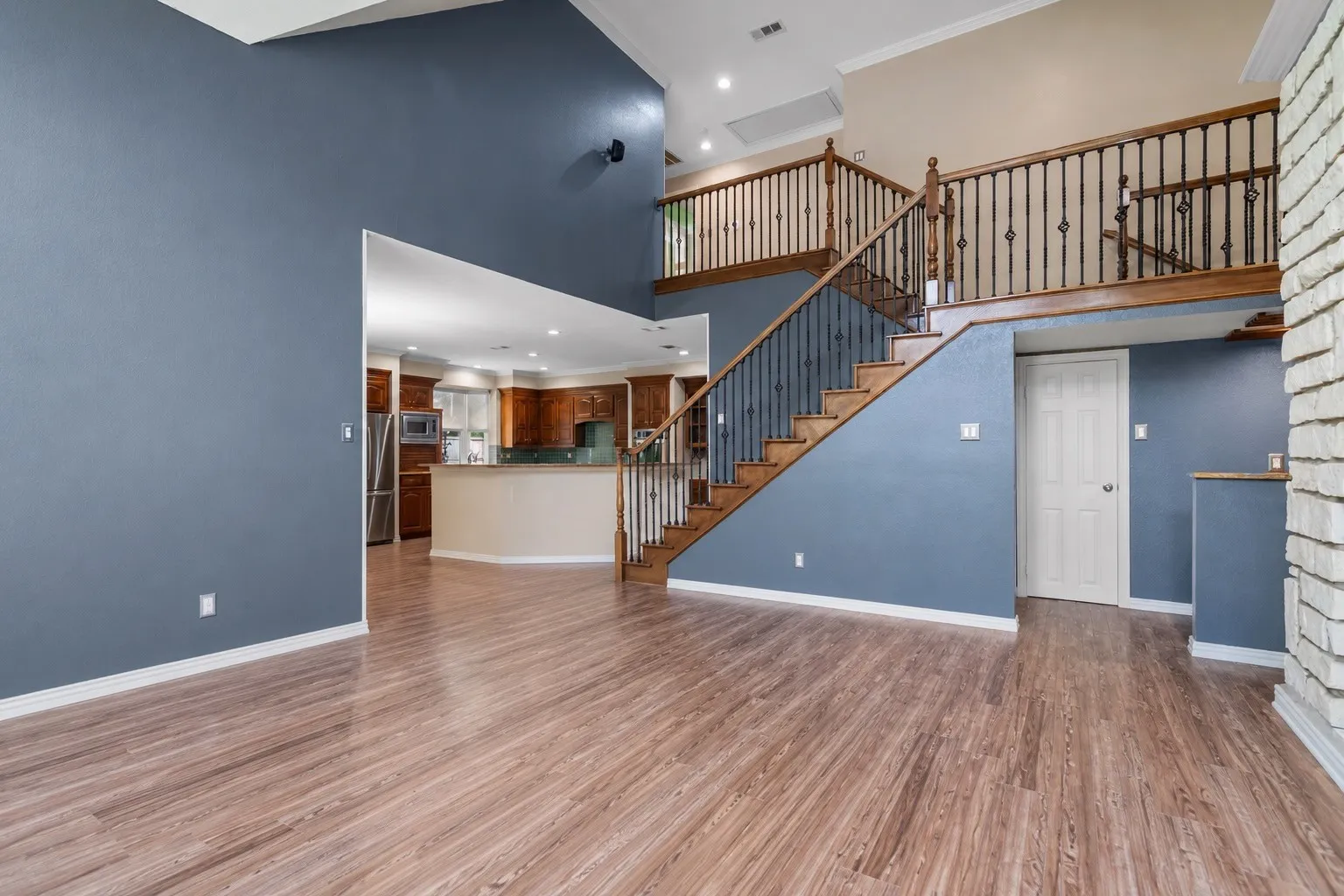 Open-concept living space featuring wood-finish flooring, a two-story ceiling, and a prominent staircase with dark iron balusters and wood handrails
