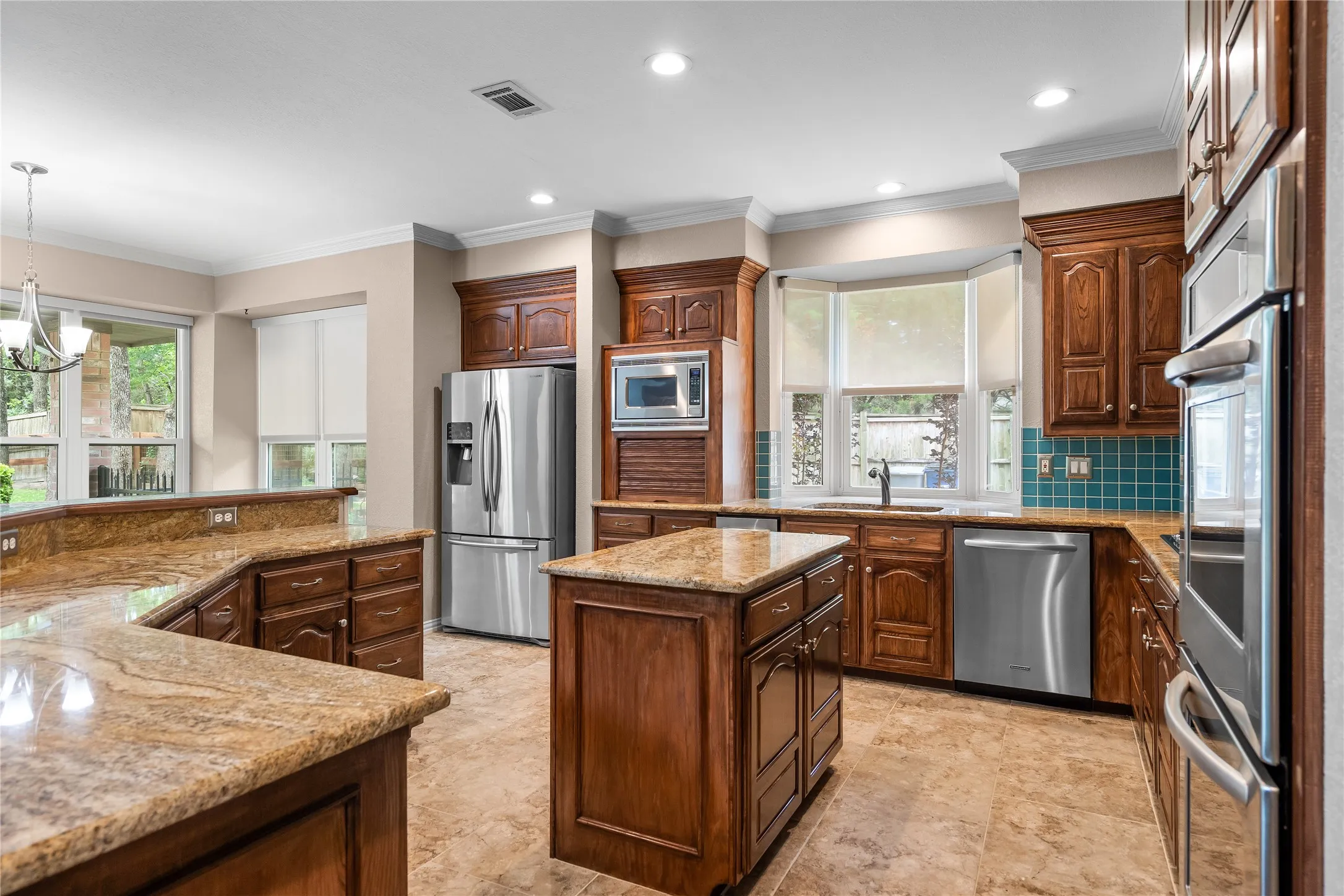 Spacious kitchen featuring warm wood cabinetry, granite countertops, stainless steel appliances, a central island, and a bay window