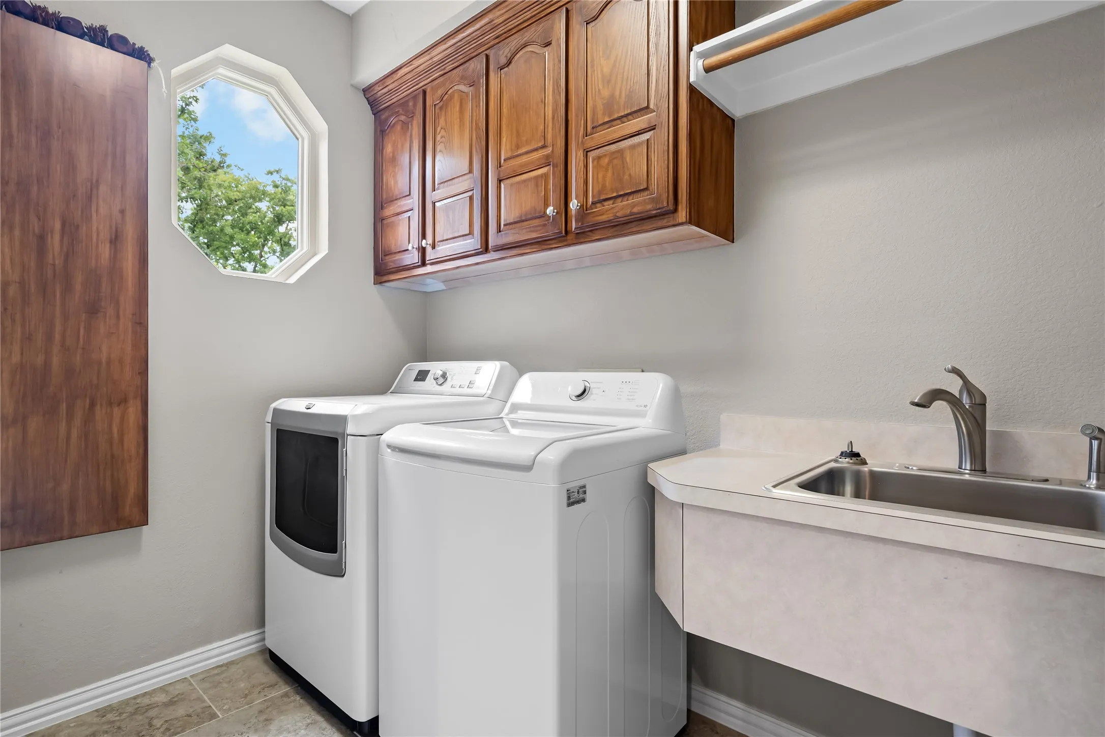 Dedicated laundry space featuring a utility sink with a brushed nickel faucet, upper cabinetry with wood-finish doors, a hanging rod, and a unique octagonal window