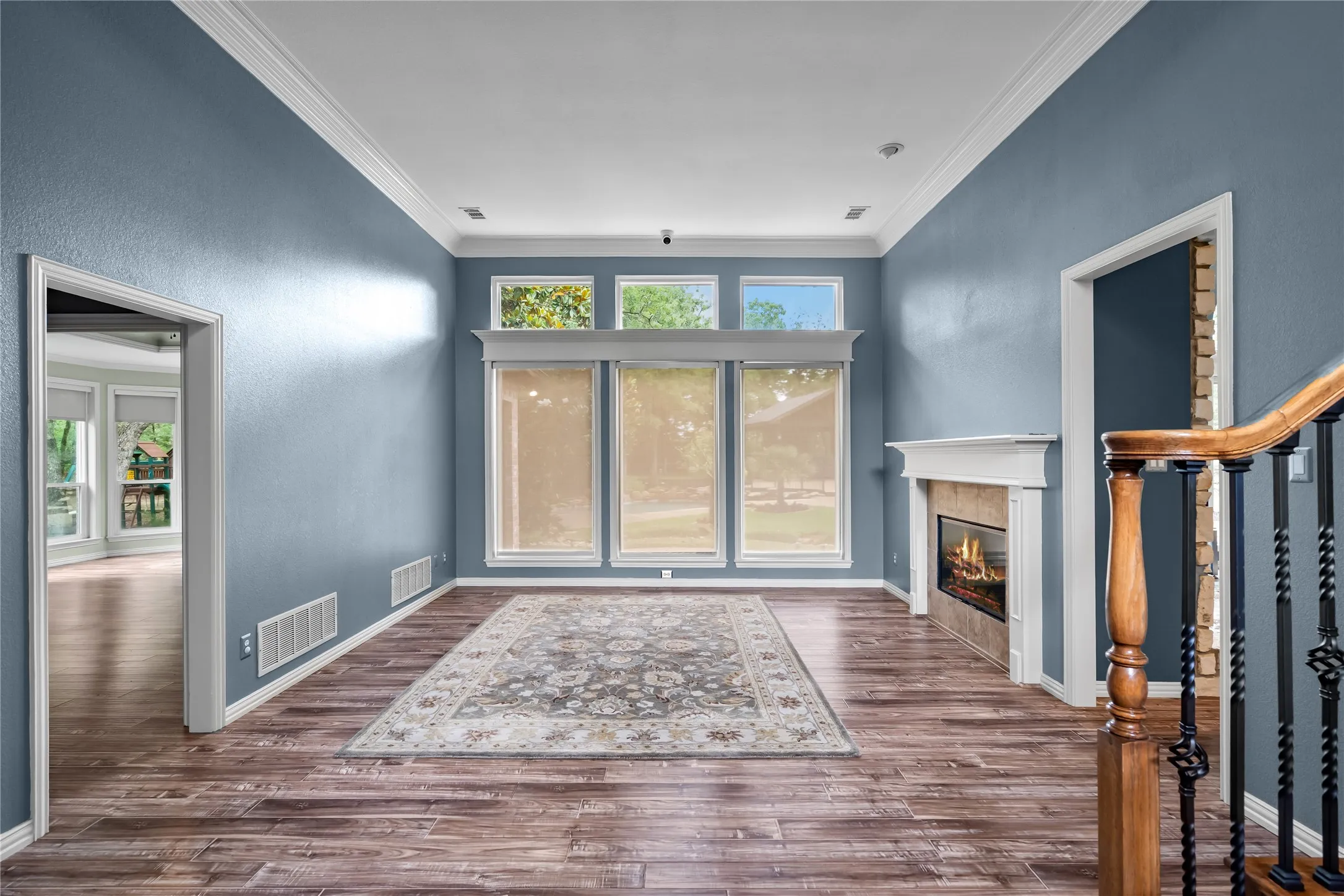 Living area featuring wood-finish flooring, a fireplace with a white mantel, and crown molding