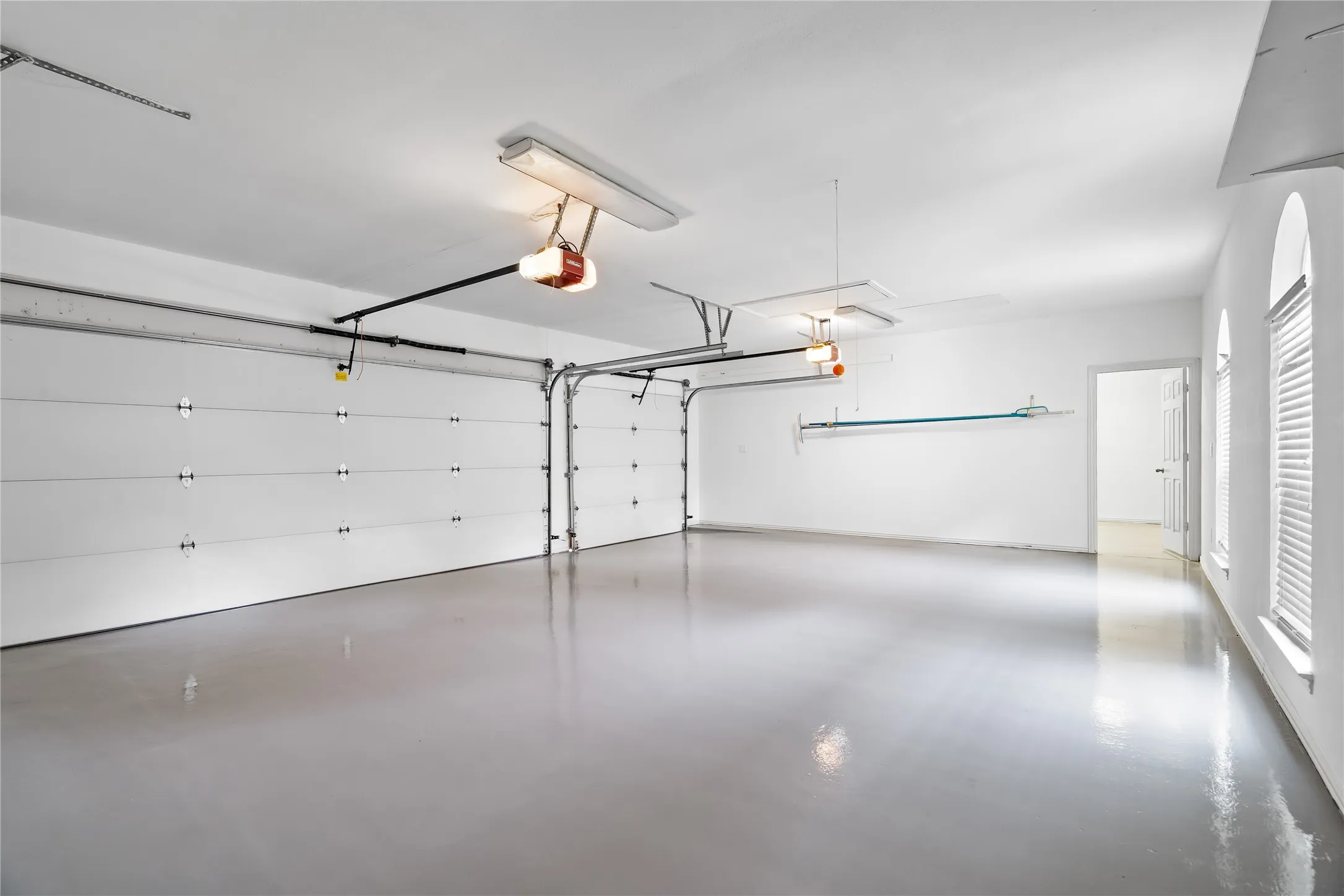 Spacious garage featuring two overhead doors, epoxy-coated flooring, multiple light fixtures, and arched windows