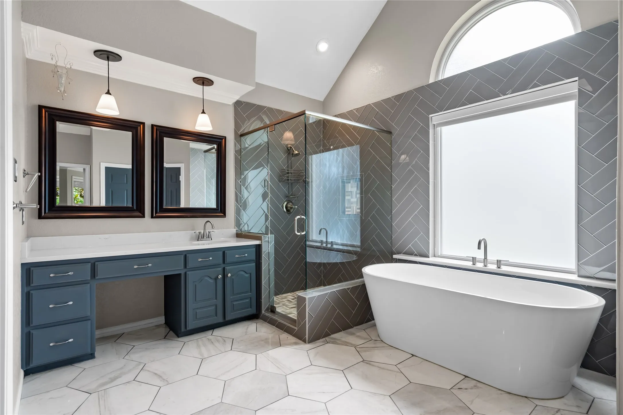 Bathroom featuring a freestanding soaking tub, glass-enclosed shower with herringbone tile, dual vanity with white countertop, and hexagonal floor tile