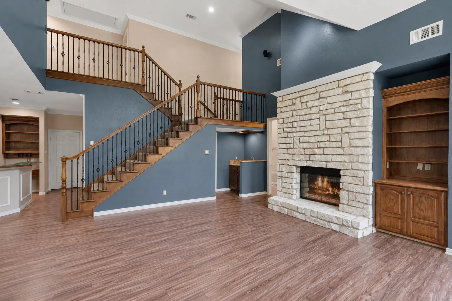 Two-story living area featuring a stone fireplace, wood-finish flooring, and a grand staircase with wrought iron balusters