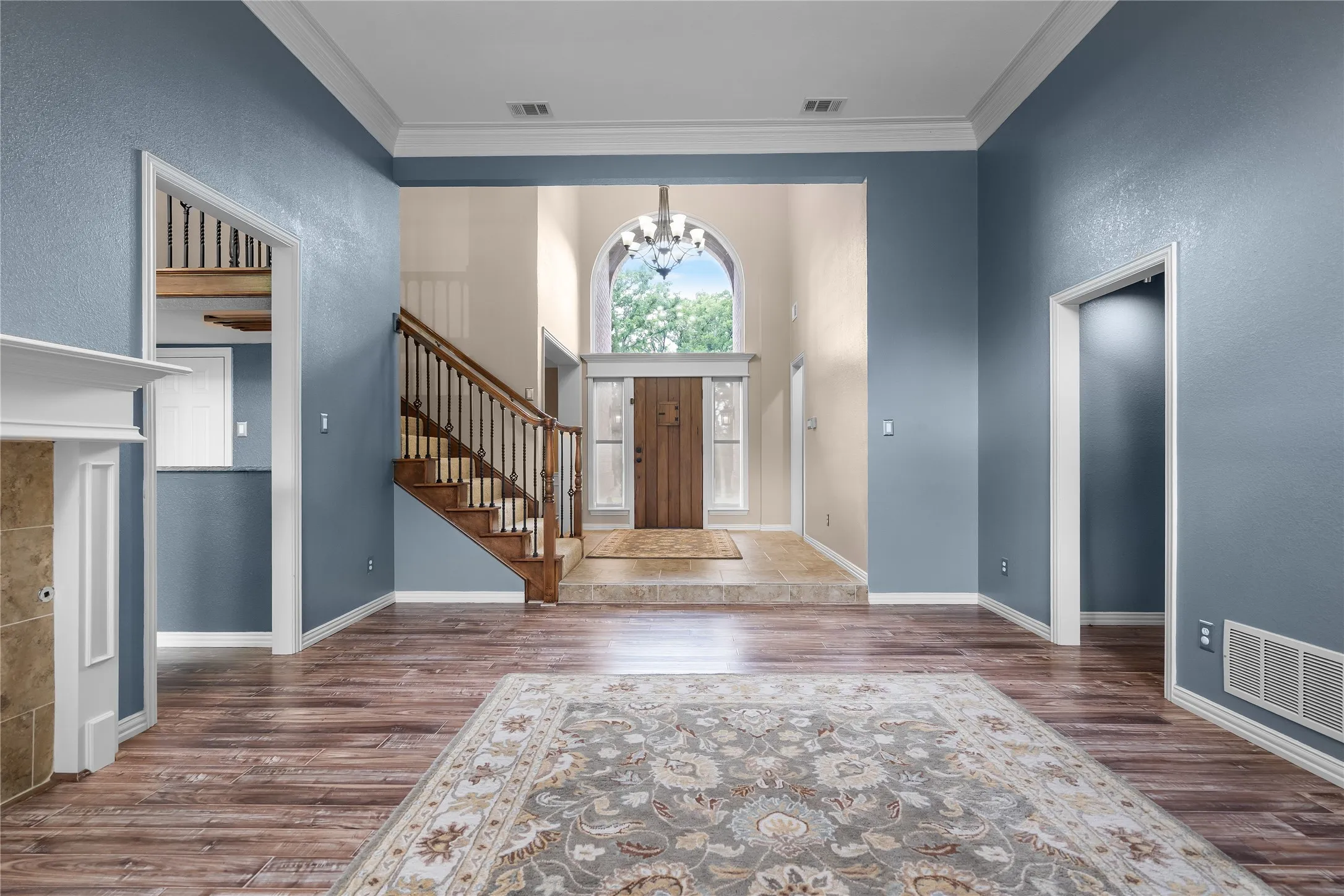 Spacious interior featuring wood-finish flooring, a grand two-story foyer with an arched window, and a prominent staircase with wood railing