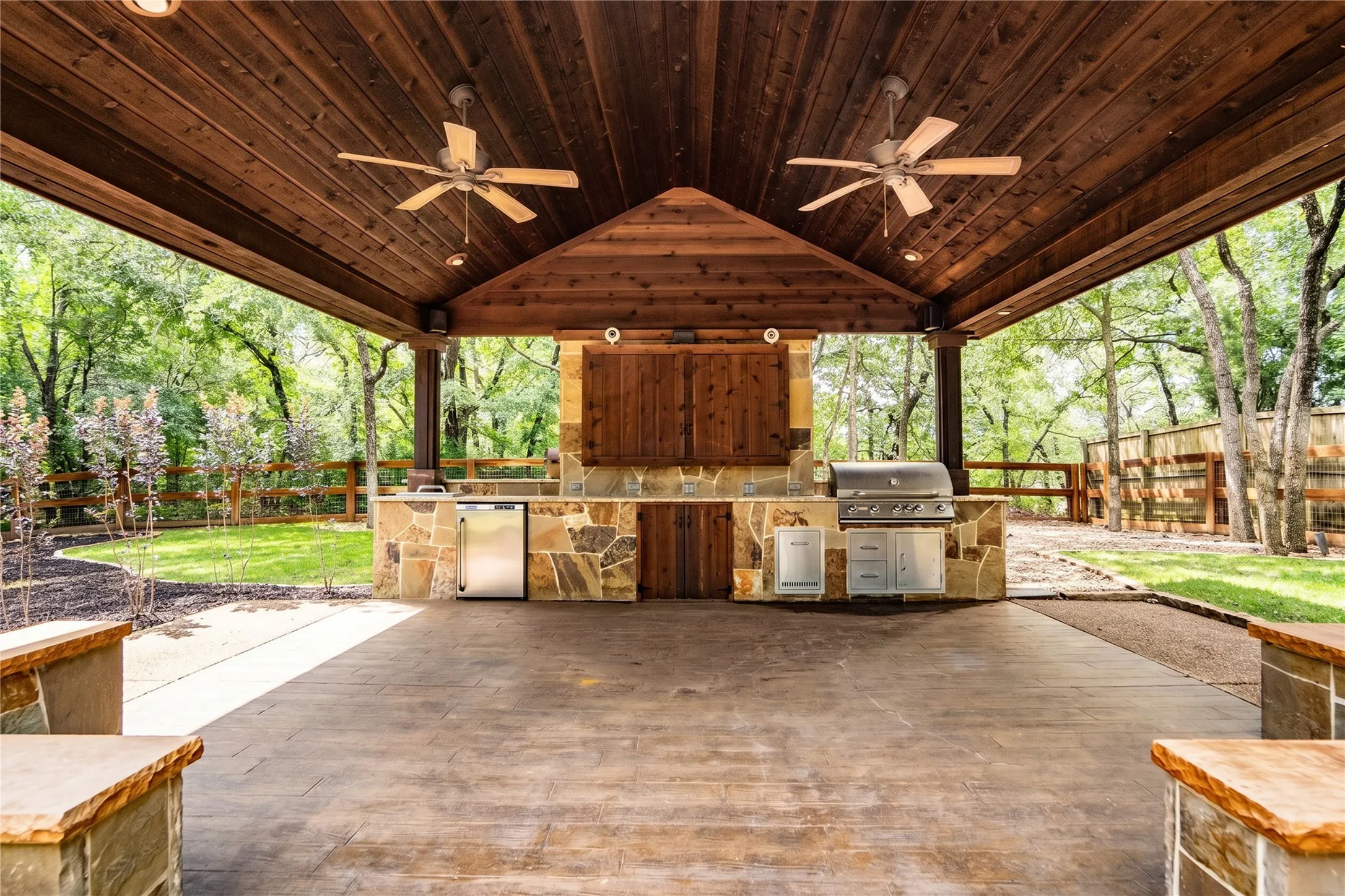 Covered outdoor living space featuring a stained wood plank ceiling with recessed lighting and two ceiling fans