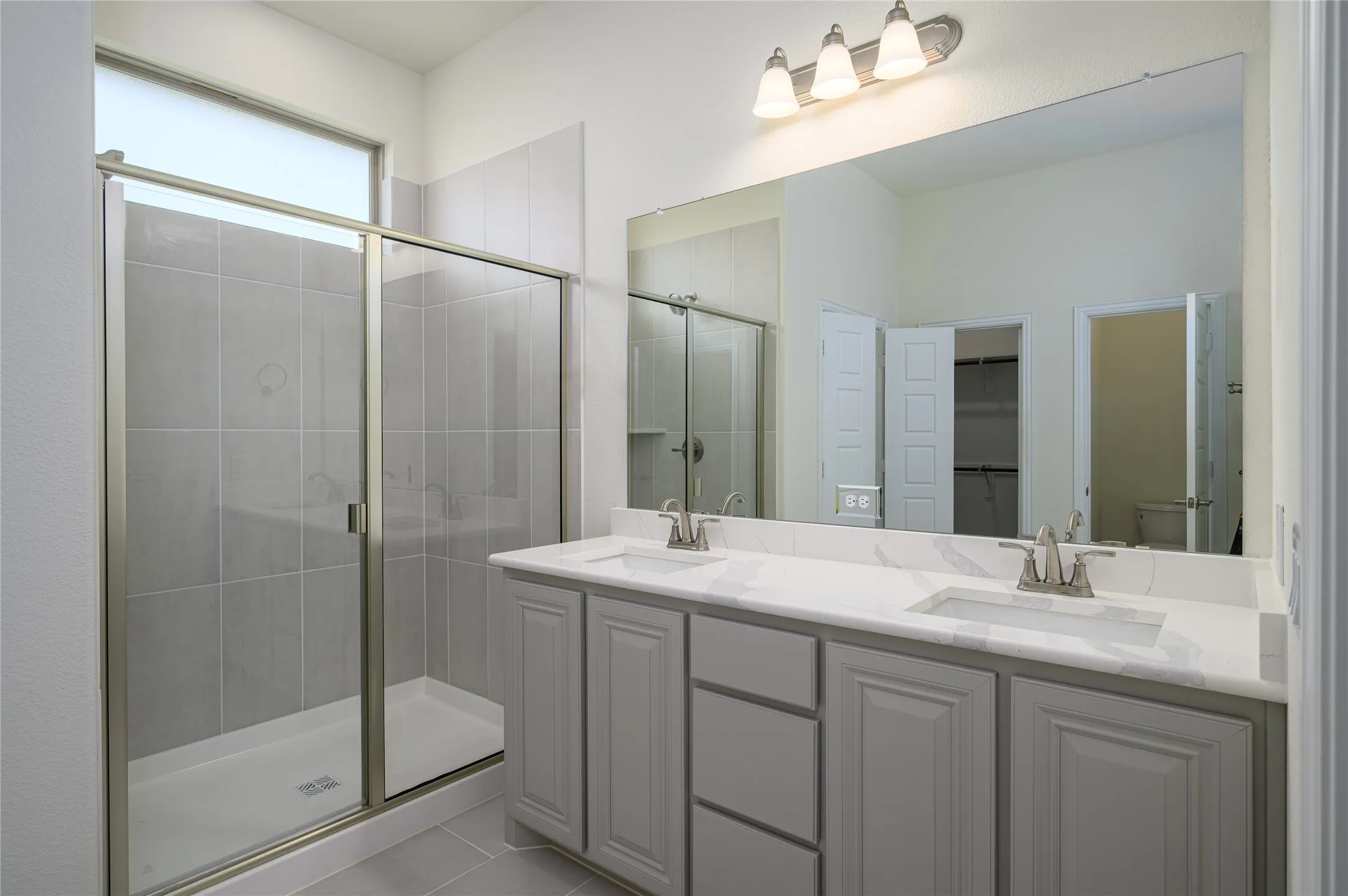 Bathroom featuring walk in shower, tile patterned flooring, toilet, and double sink vanity