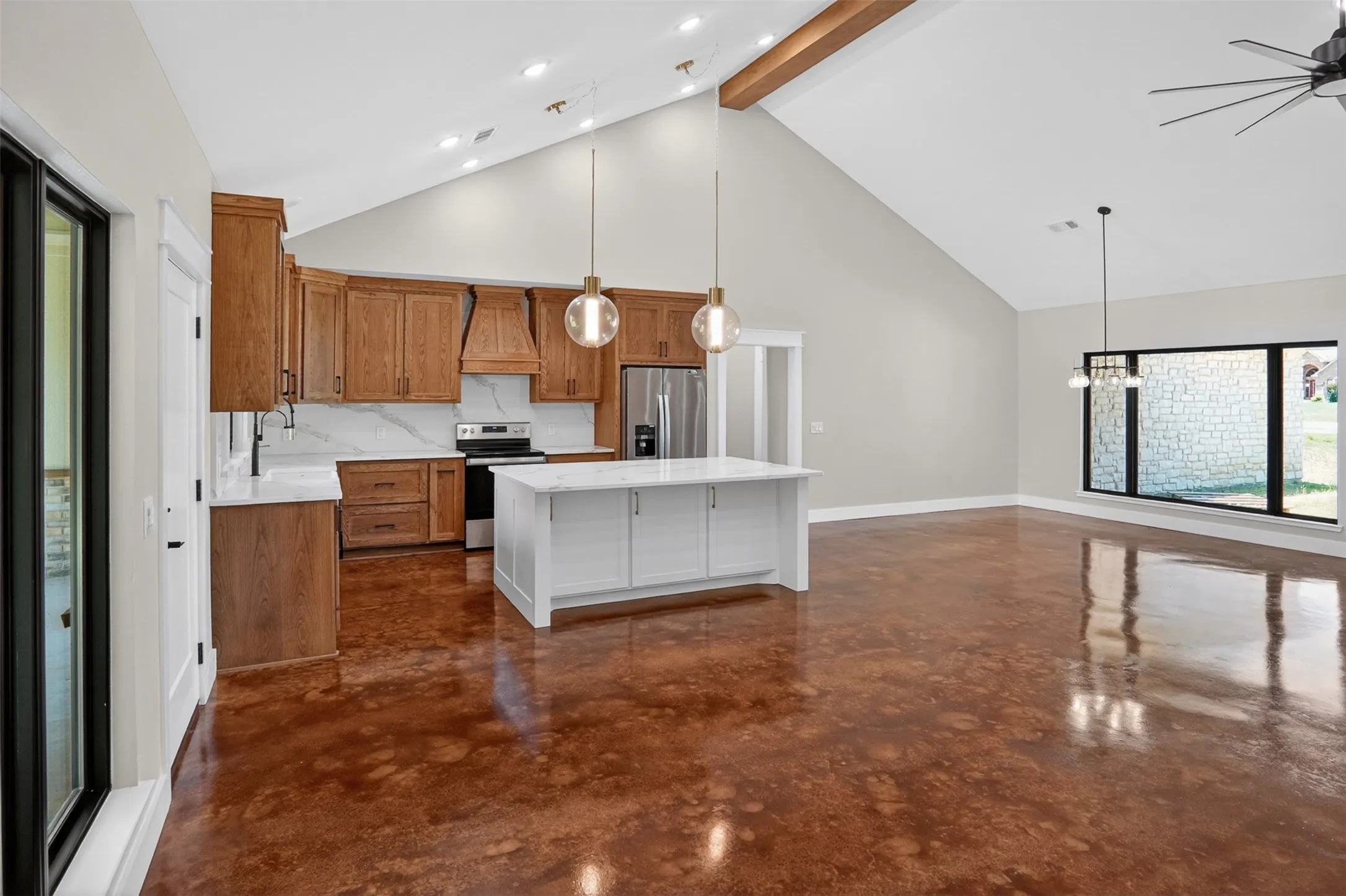 Open concept living area featuring a vaulted ceiling with exposed wooden beam, stained concrete flooring, and a kitchen with wood cabinetry and a central island