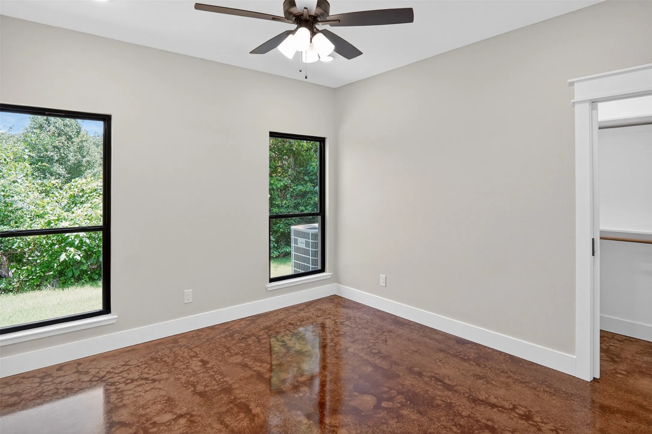 Bright room featuring two large windows with black framing, a ceiling fan, and concrete flooring