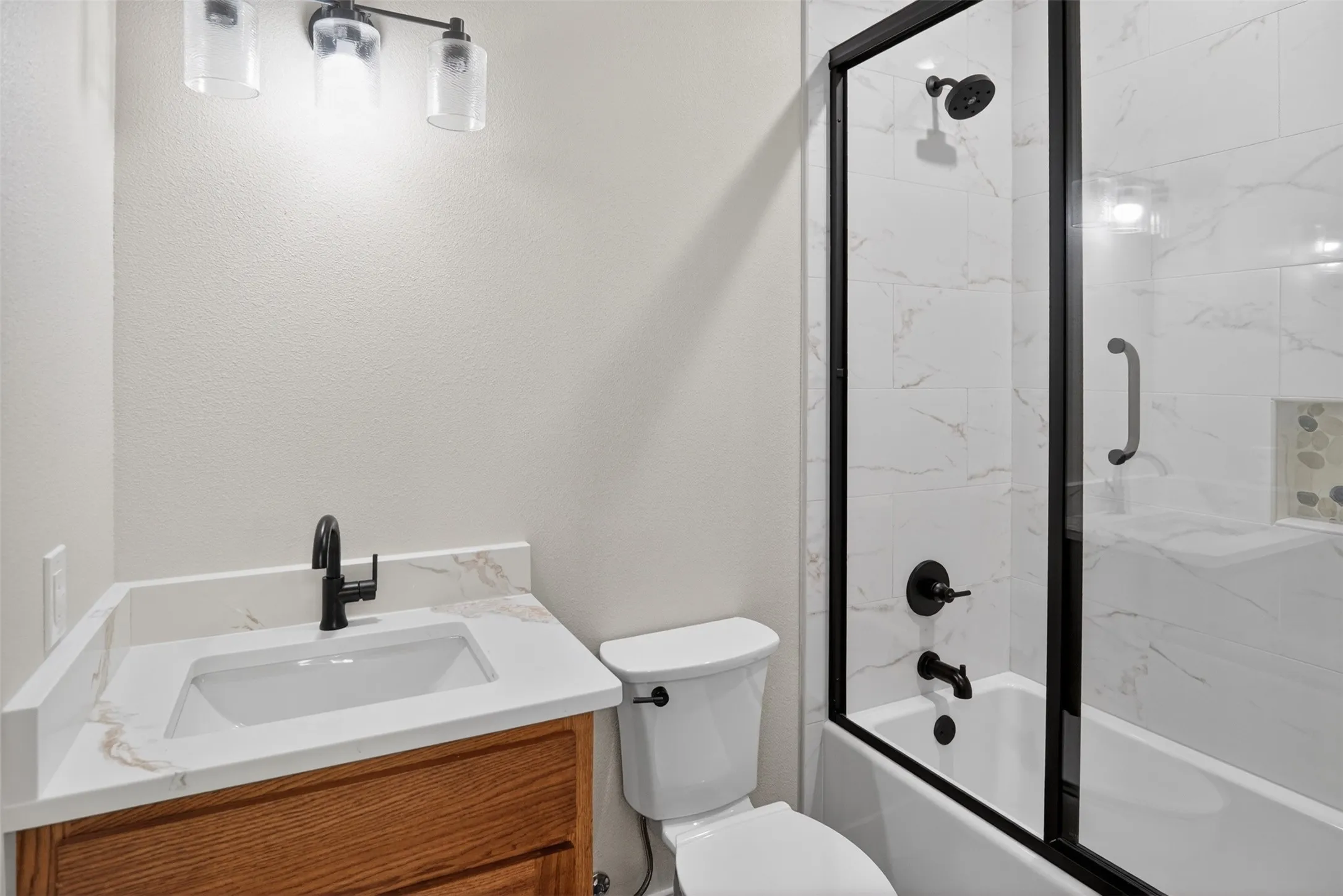 Ensuite Bathroom to 2nd primary featuring a single-sink wood-finish vanity with a light-toned countertop, matte black faucet, and three-light vanity fixture