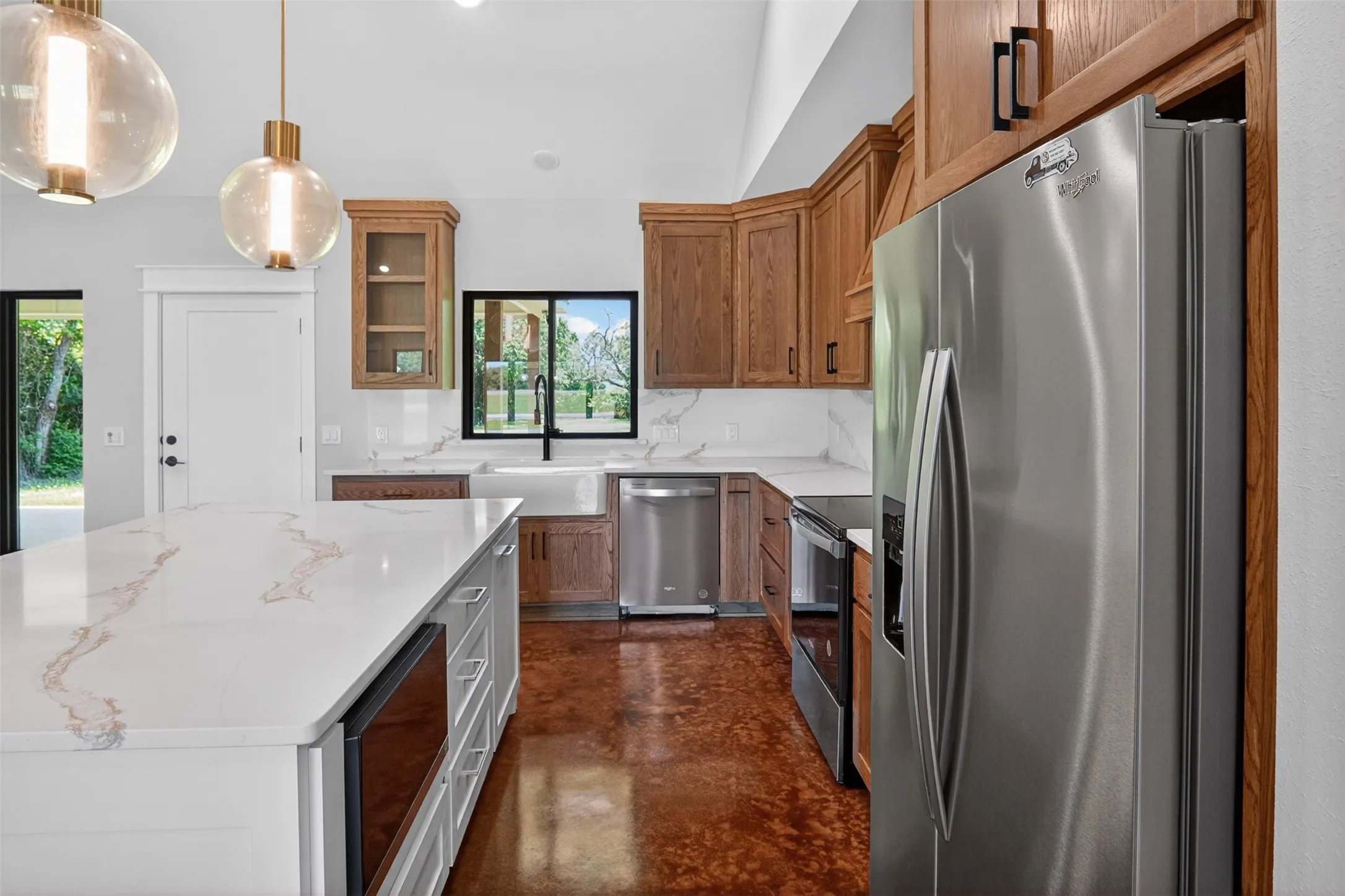 Kitchen featuring a large central island with a light-toned countertop, wood-finish cabinetry, stainless steel appliances, and a farmhouse sink