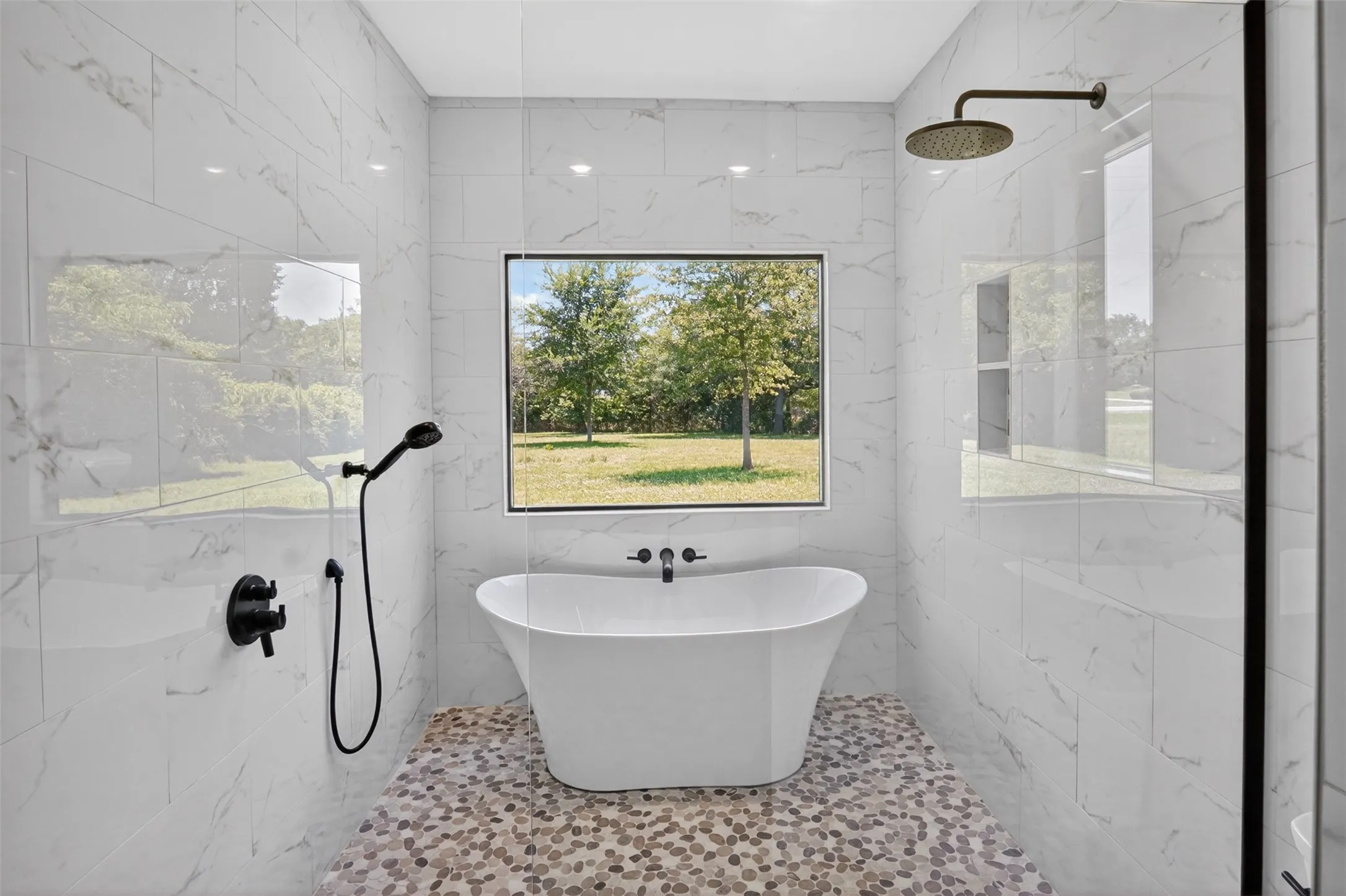 Primary Modern bathroom featuring a standalone soaking tub with wall-mounted faucet, matte black fixtures, pebble-tile flooring, and large format white tile walls