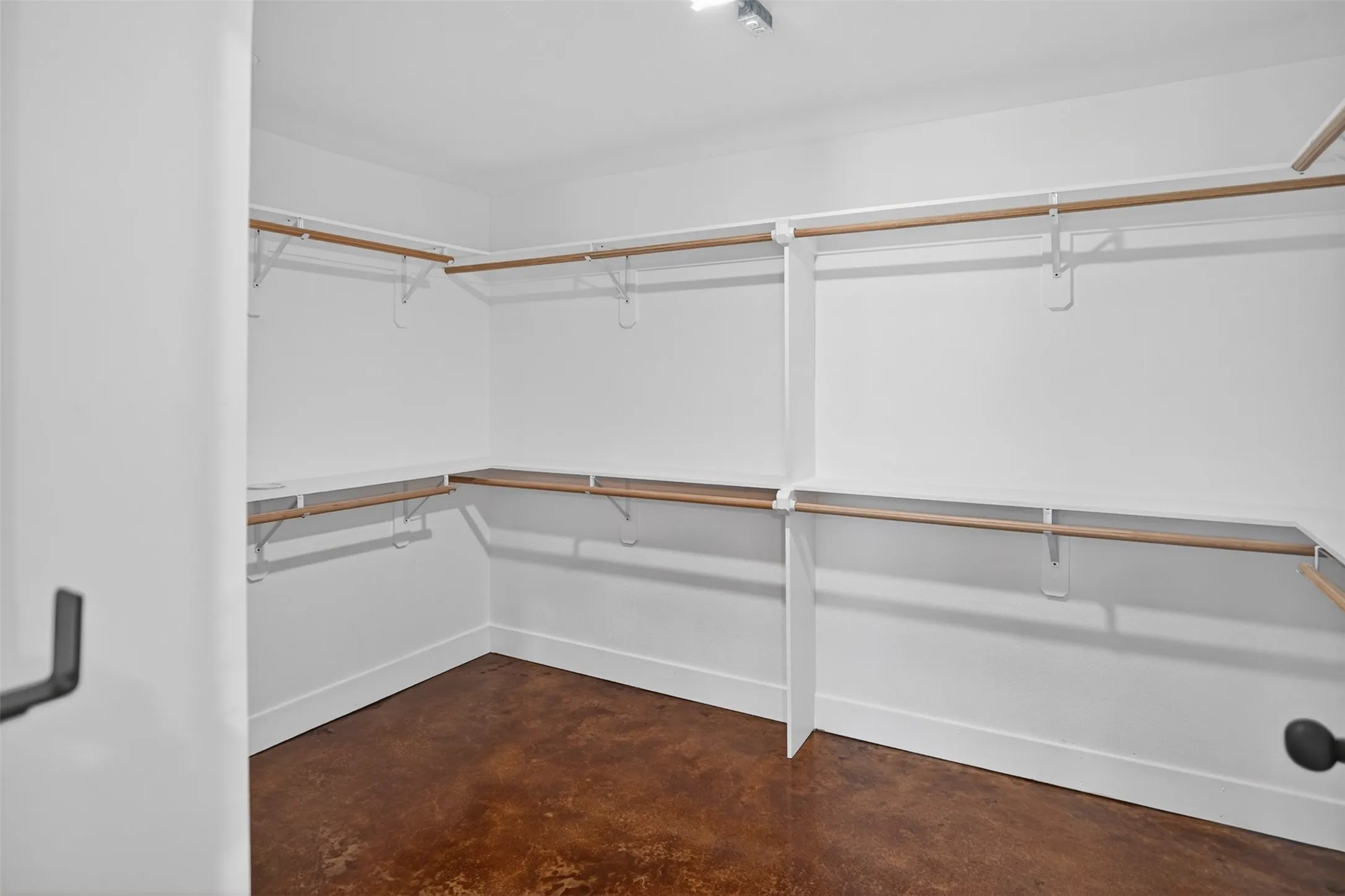 Safe room/ primary walk-in closet featuring an integrated shelving system, multiple hanging rods, white walls, and a dark, textured floor
